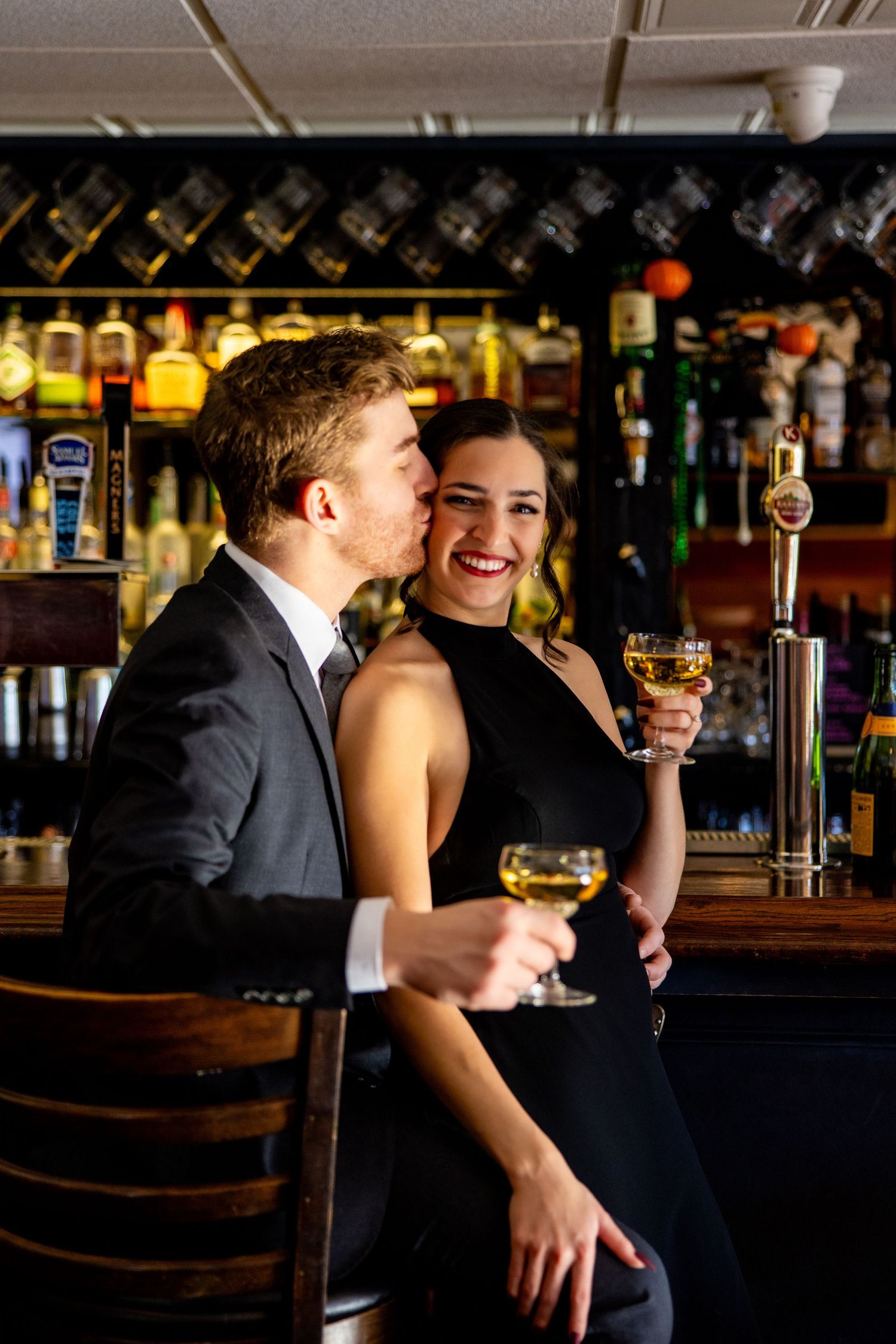 Couple in formal wear sharing wine and intimate moments at a bar.