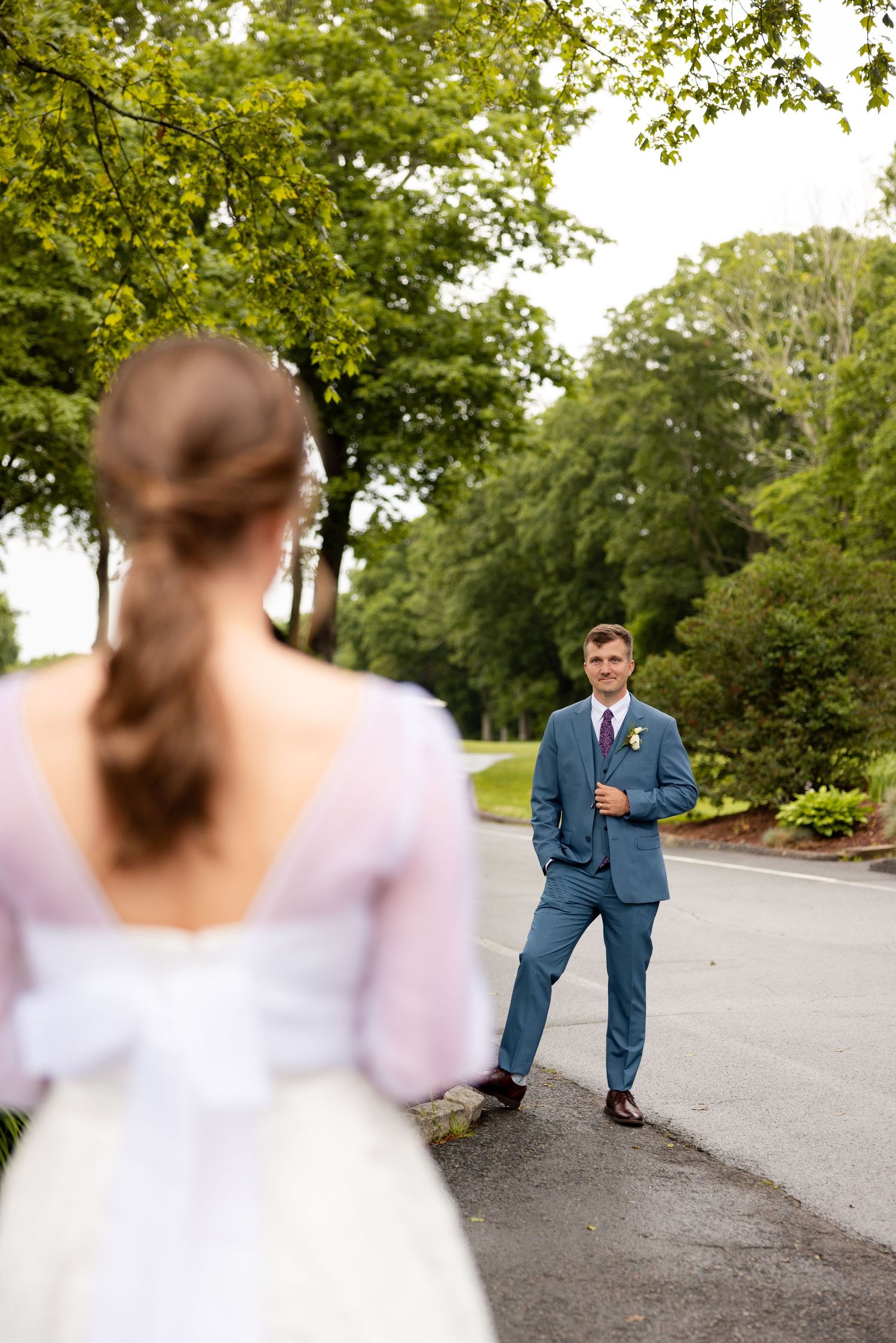 A romantic first look moment between a couple captured on a winding tree-lined road during an outdoor wedding photoshoot.
