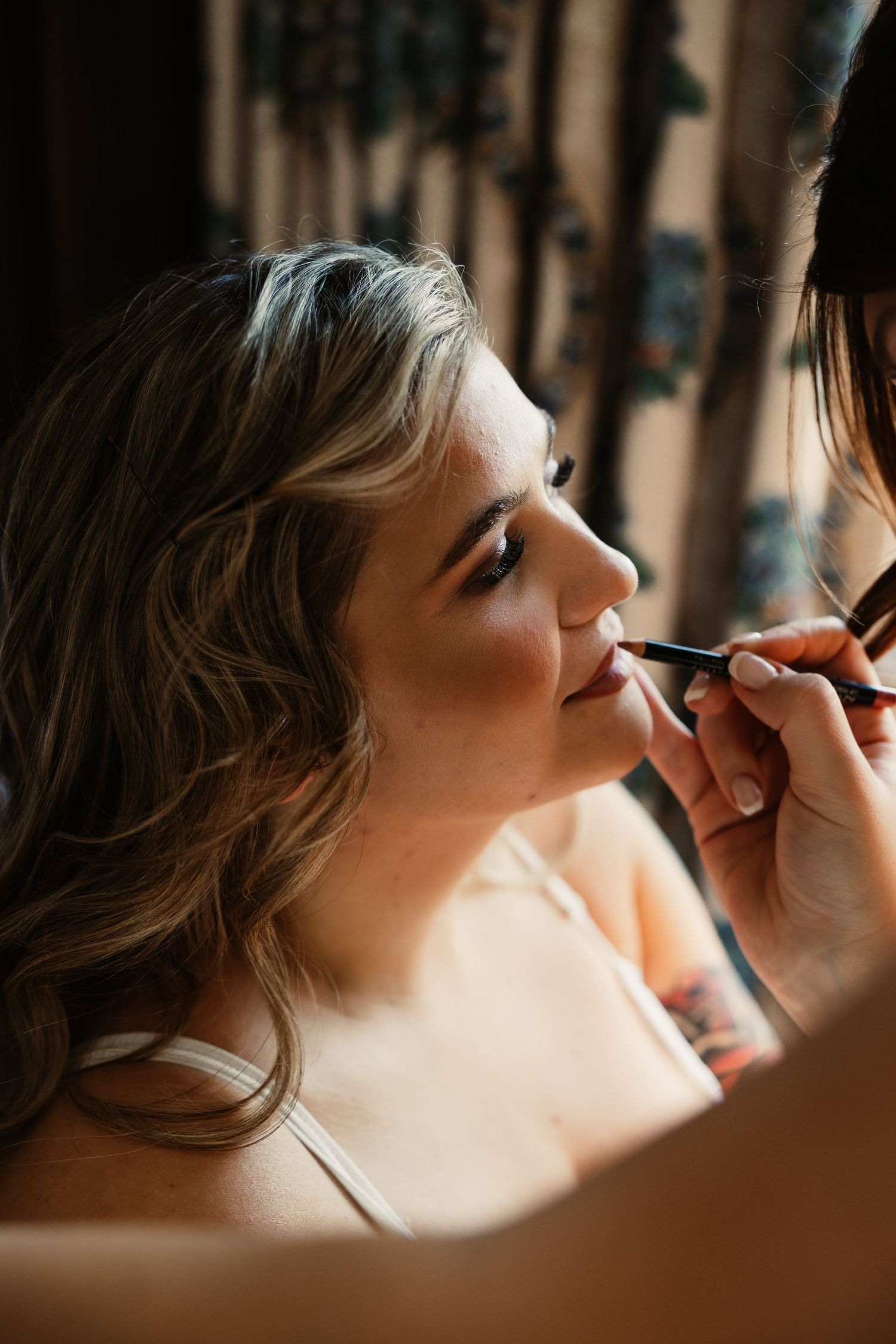 Makeup artist applying cosmetics on a client's face in warm lighting.