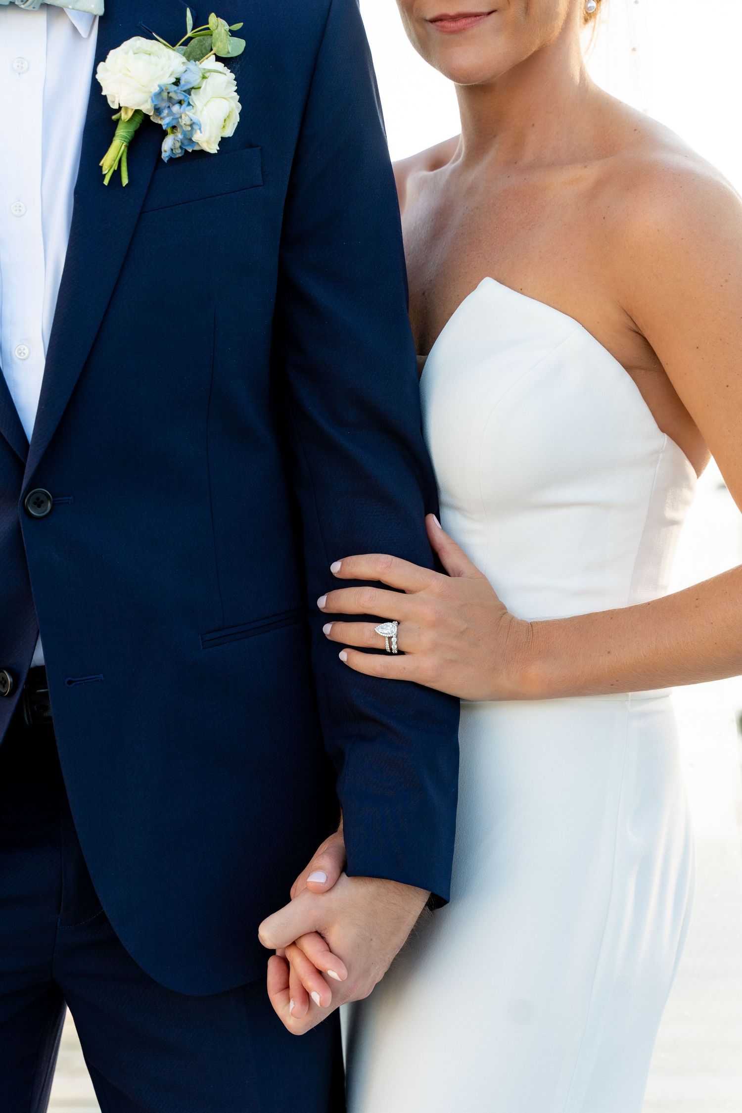 Close-up of bride in strapless gown and groom in navy suit showing wedding details.