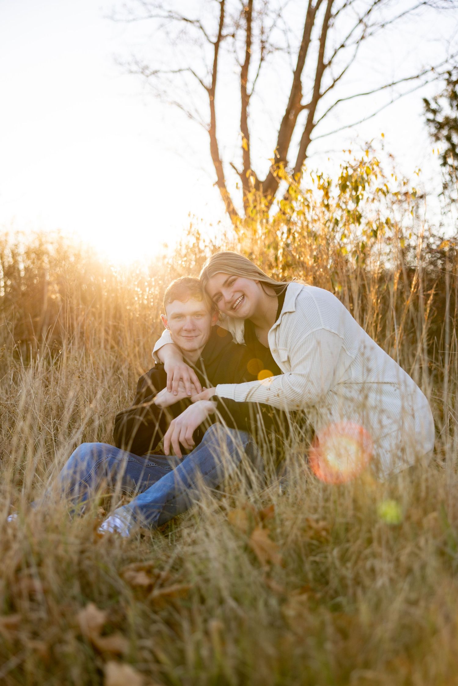 Candid moment between couple sitting in tall grass during golden hour.