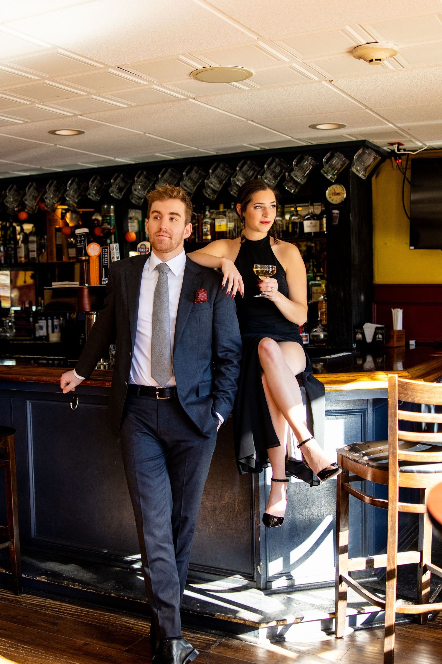 Stylish couple poses at bar counter in upscale pub setting.
