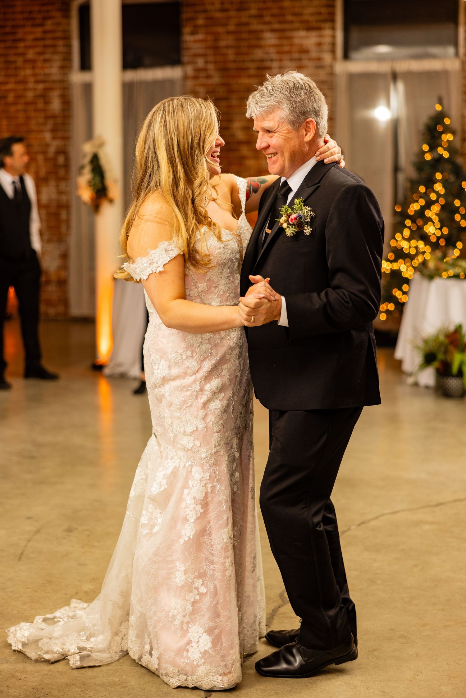 A couple dances together during their wedding reception with glowing Christmas lights in the background.