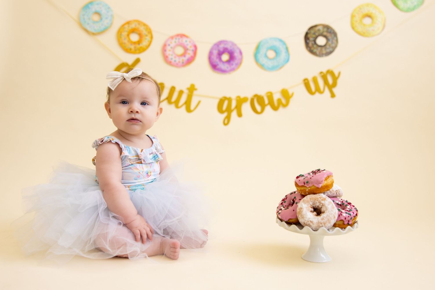Baby in tutu dress with donut decorations and party banner in background.