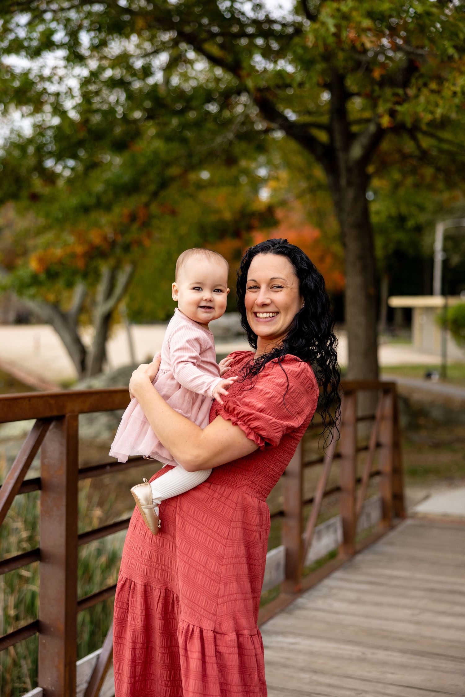 A joyful autumn moment shared on a wooden bridge while wearing coordinating pink and red outfits.