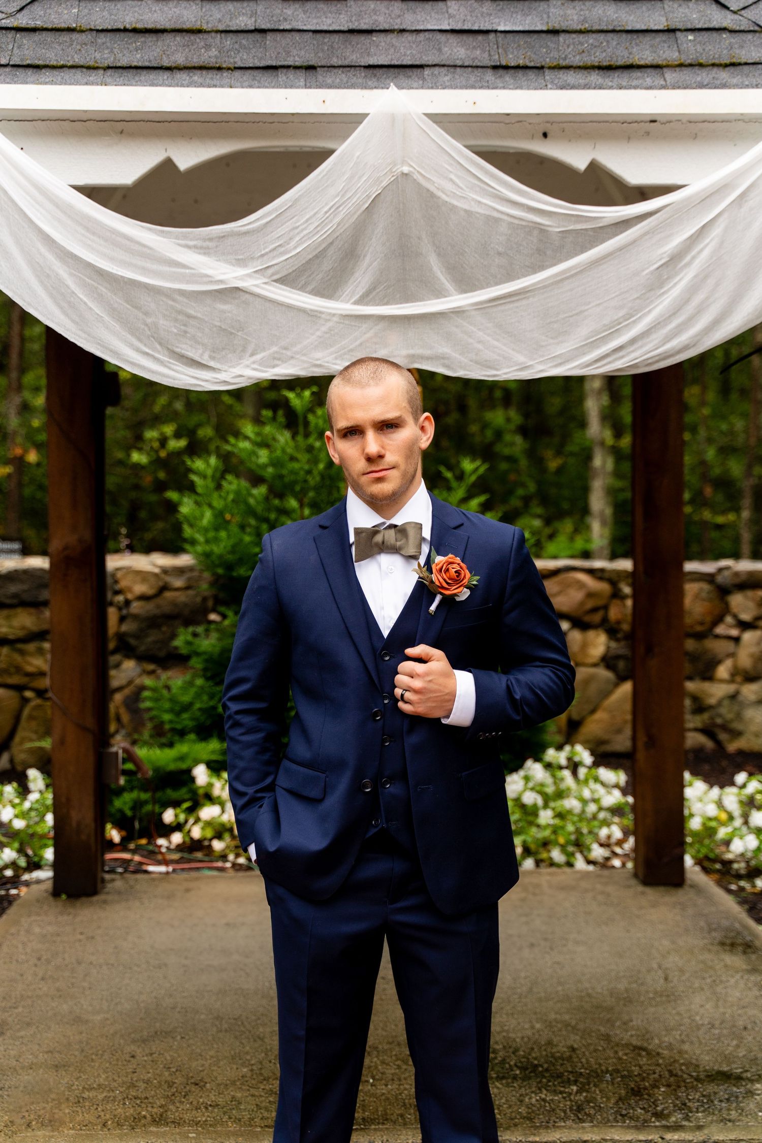 Wedding ceremony gazebo decorated with white fabric draping and stone wall background.