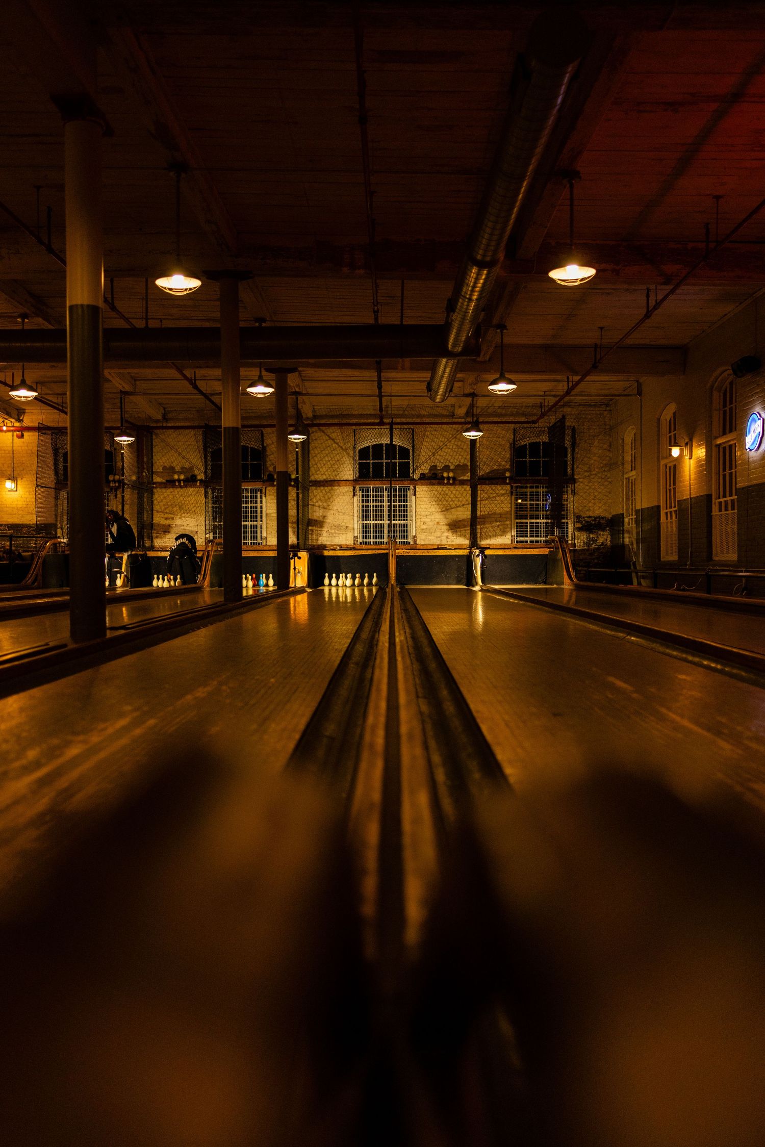 Vintage bowling alley lane illuminated by warm overhead lights creating dramatic shadows.