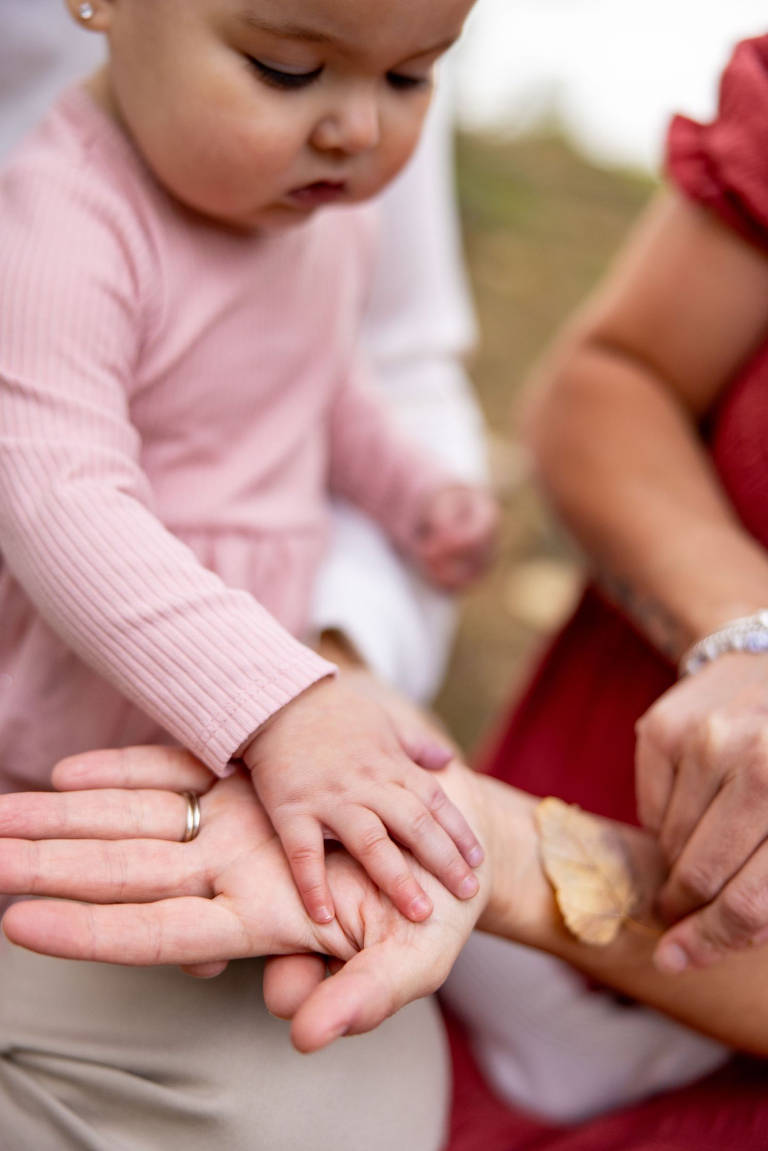 Close-up of baby's hand resting on parent's palm in outdoor setting.