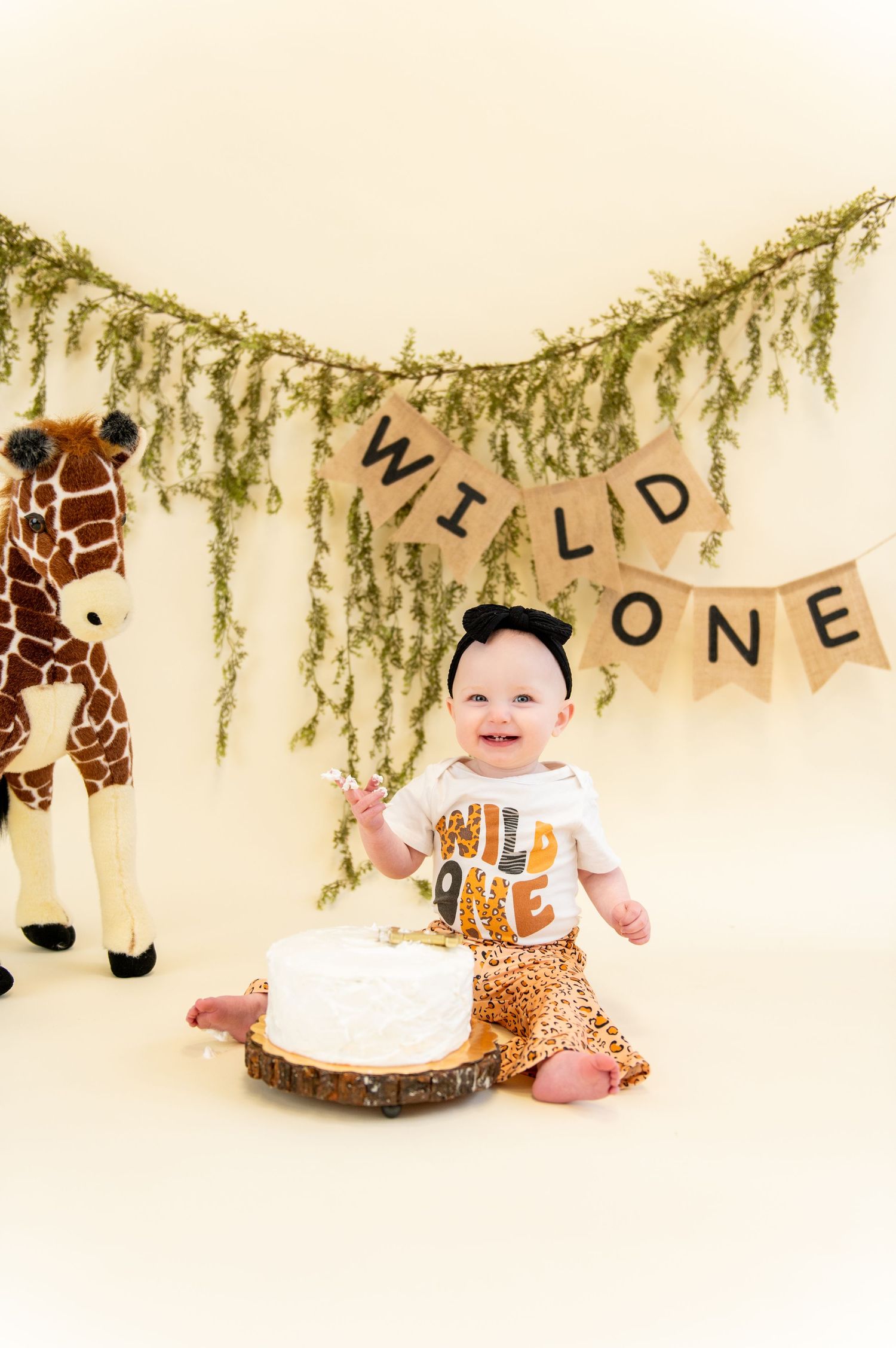 Safari themed first birthday setup with greenery garland and giraffe plush toy.