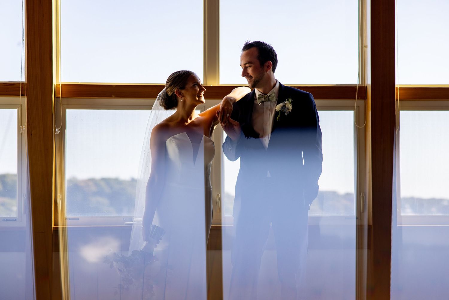 Silhouetted couple shares romantic moment against sunlit window backdrop.