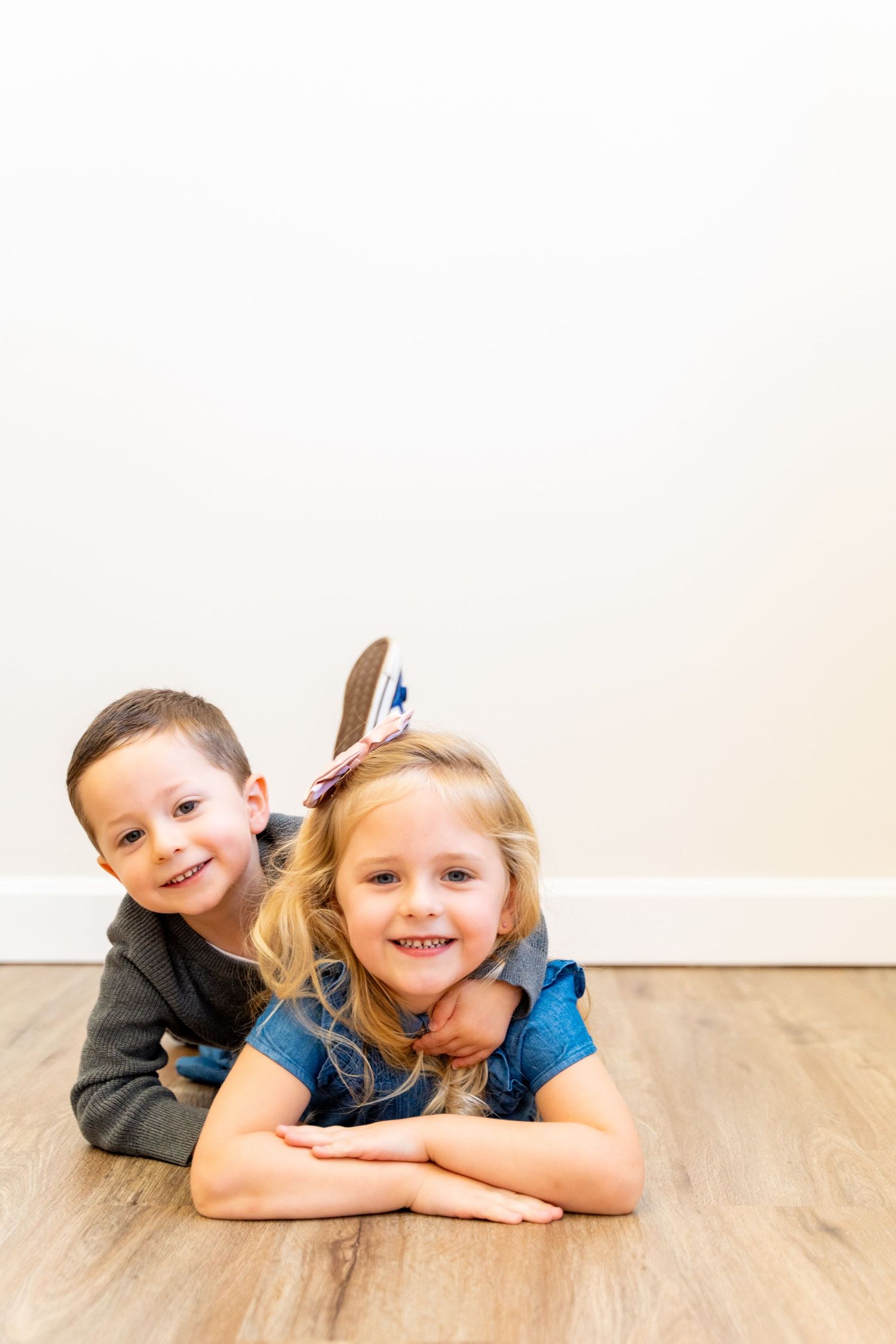 Two children lying on hardwood floor posing for camera.