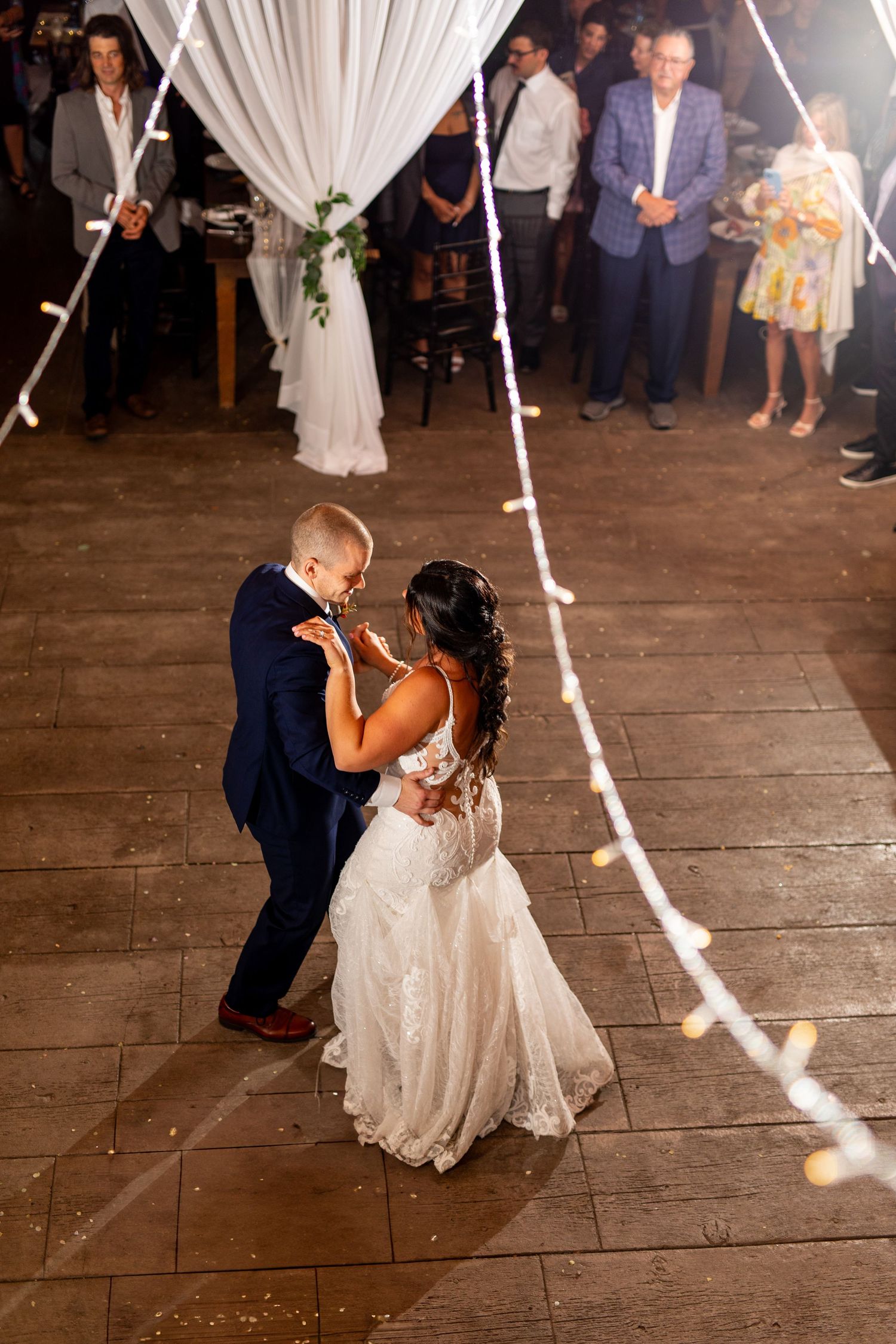 Newlyweds dance beneath elegant white drapes and string lights at their reception.