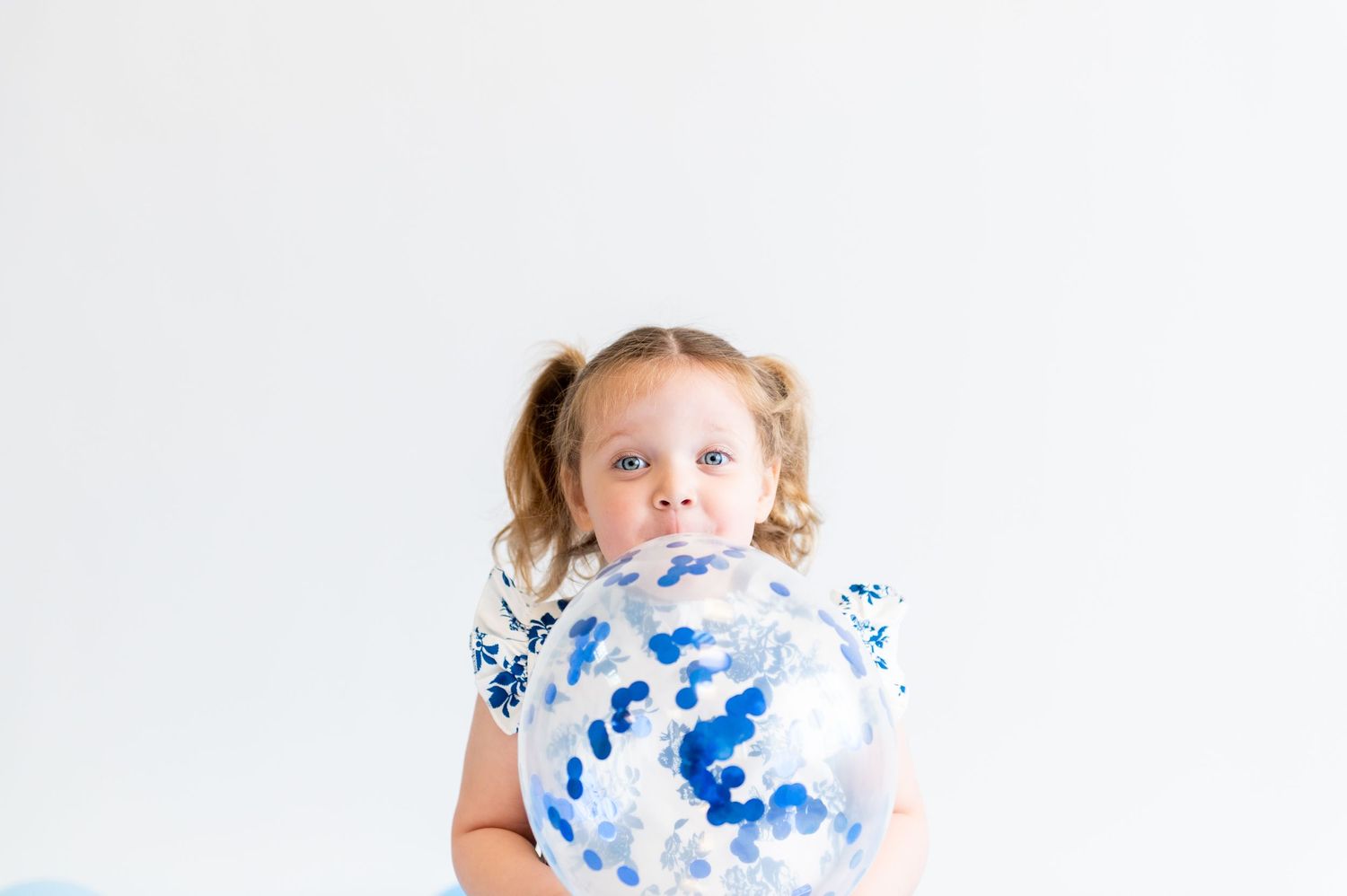 Child holding blue and white balloon against white background.