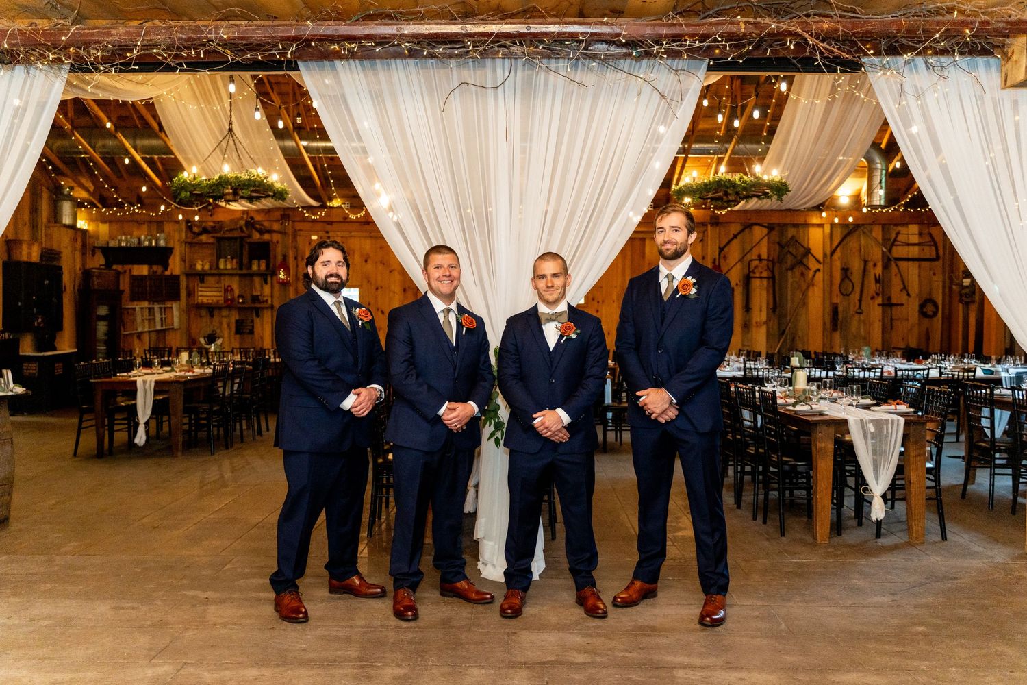 Groomsmen in navy suits and brown shoes pose in rustic barn reception venue.