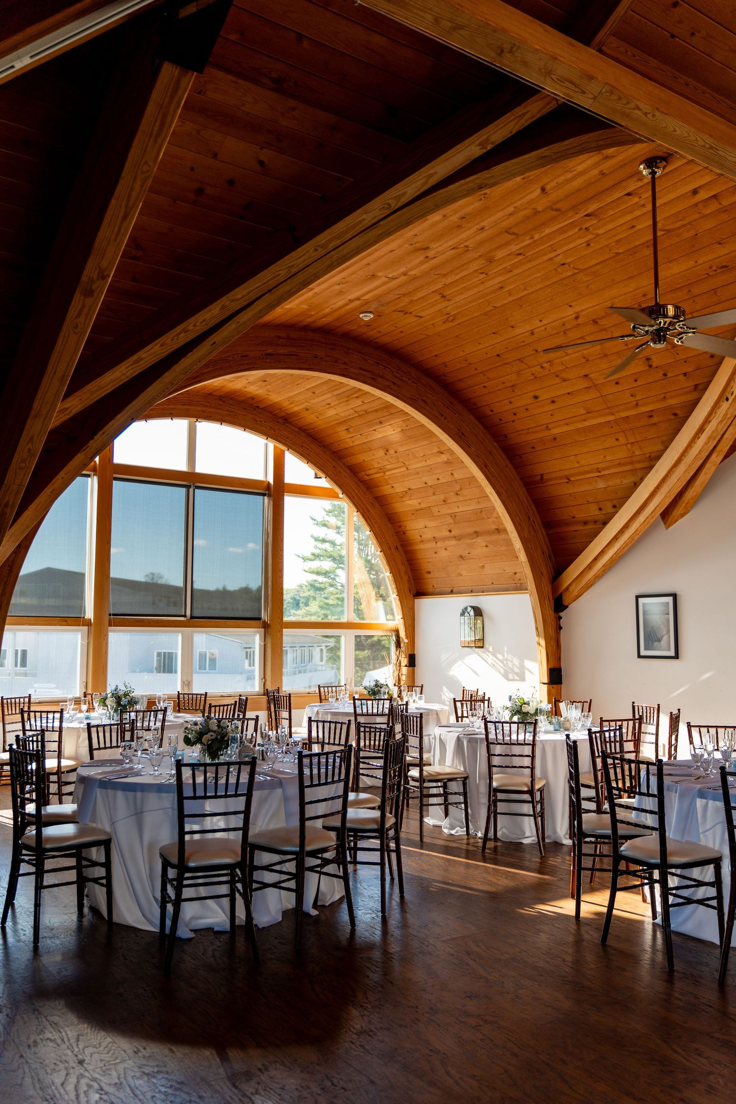 Reception venue with wooden arched ceiling, elegant table settings and Chiavari chairs.