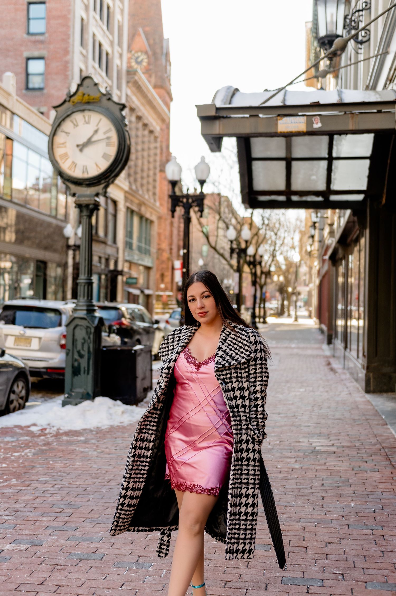 A pink silk dress and checkered coat outfit photographed on a snowy city street with vintage clock.