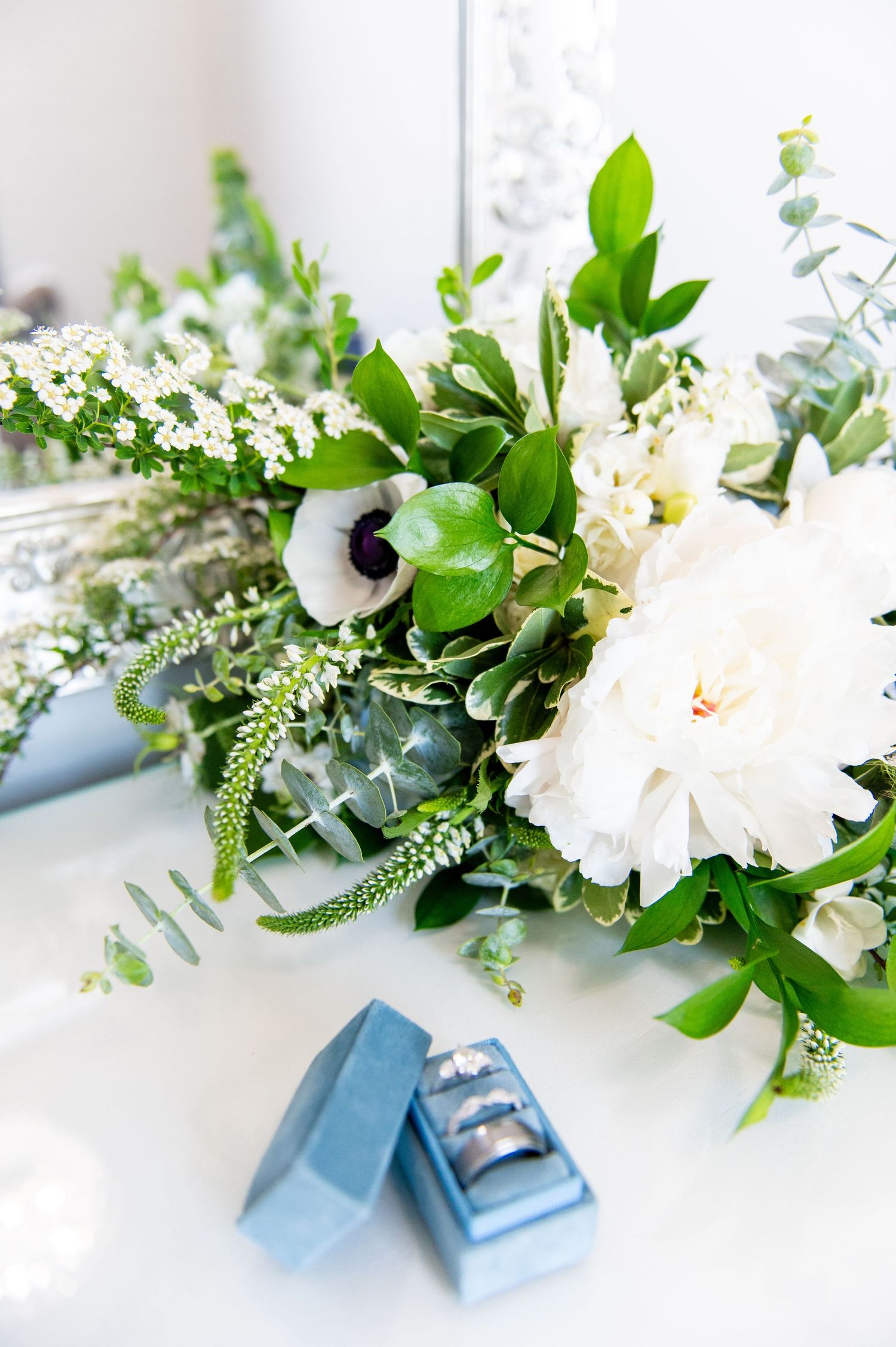 A white and green wedding bouquet with anemones and eucalyptus arranged with silver jewelry box.