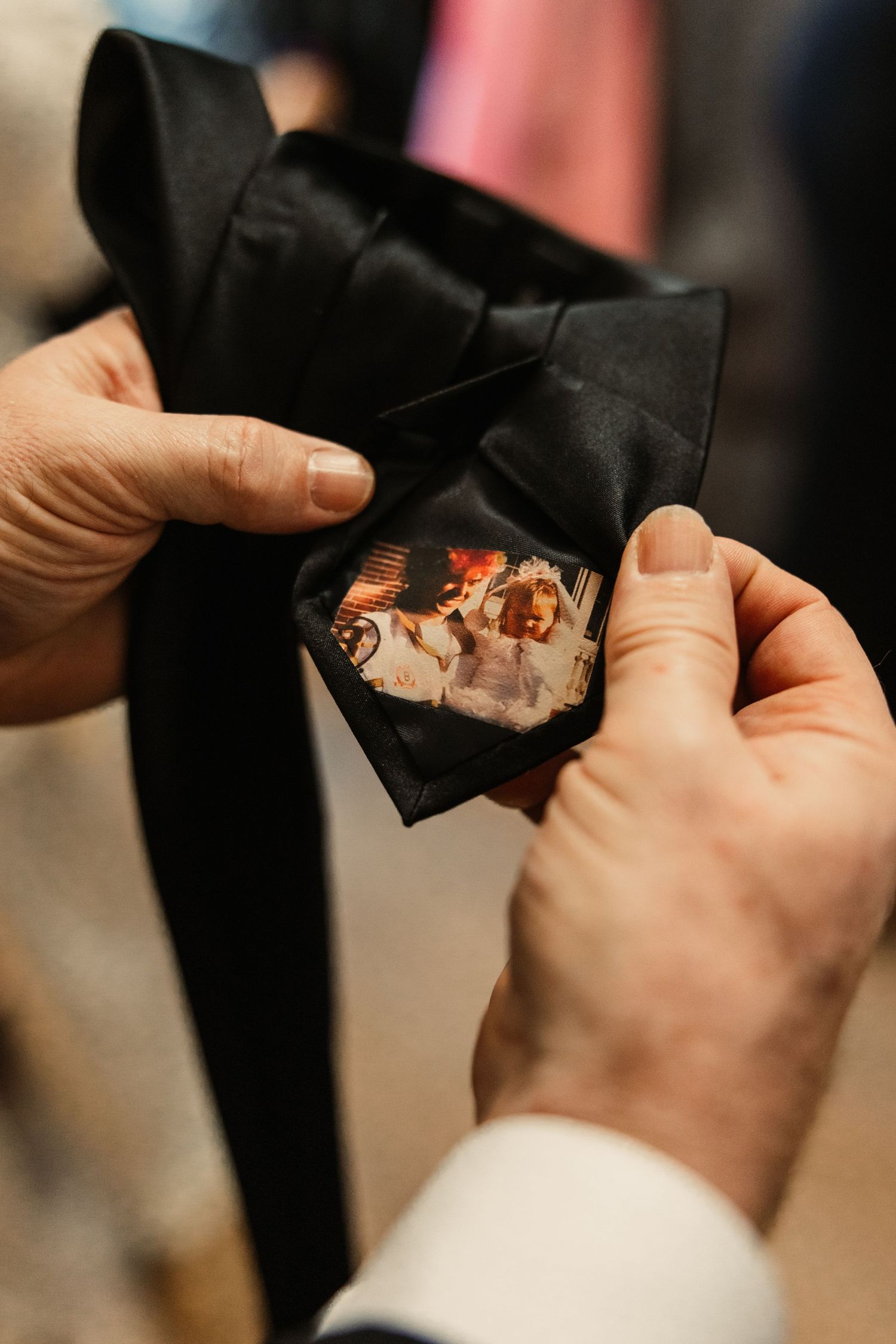 Hands holding and folding a black necktie with photo tucked inside.