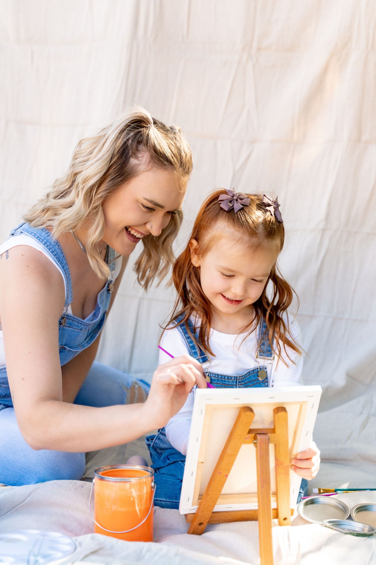 A parent and child paint together at a small easel while wearing matching denim.