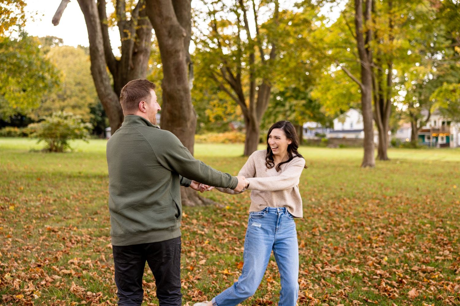 A couple dances playfully in a park covered with fallen autumn leaves.