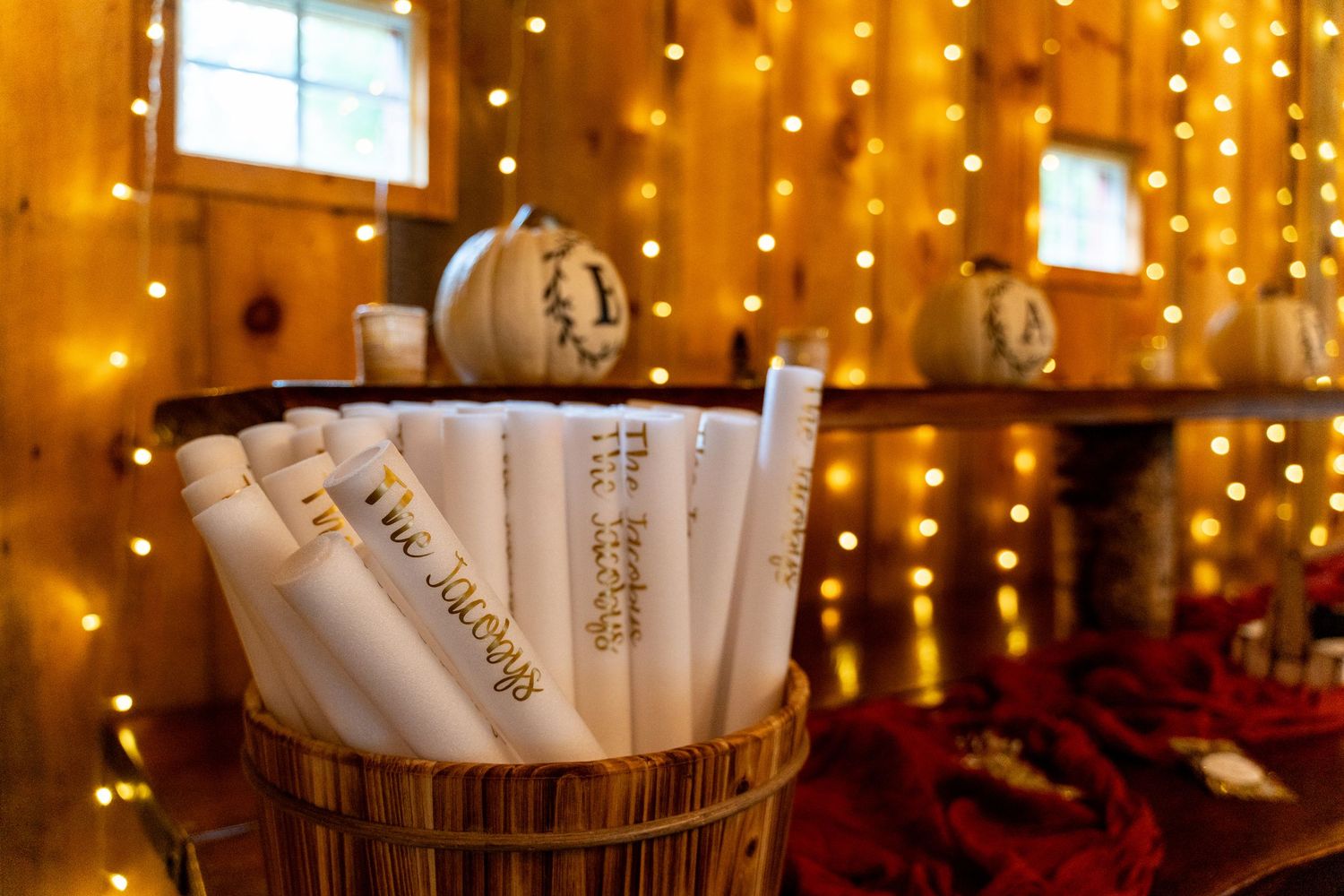 Wedding programs in wooden barrel with warm twinkle lights in background.