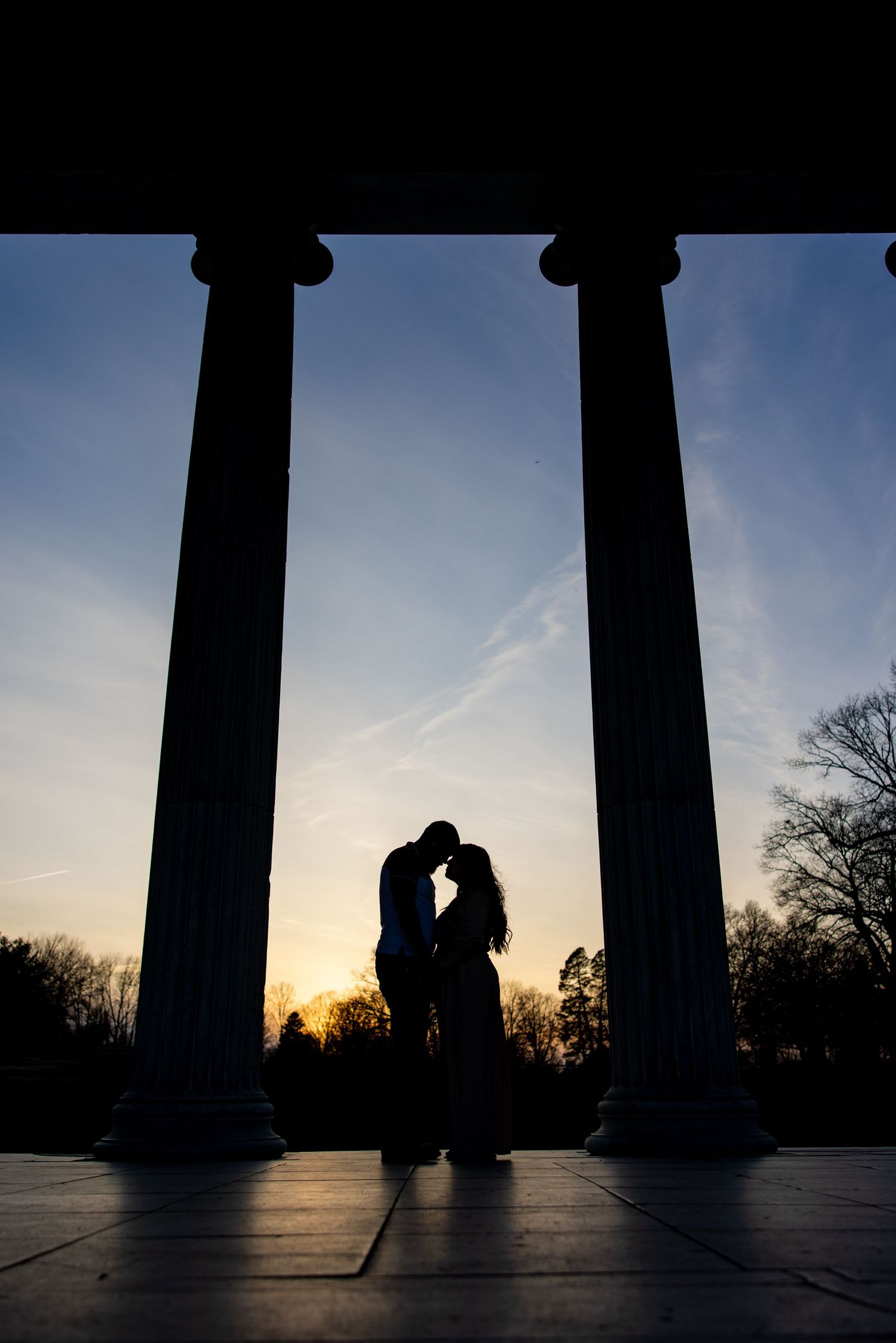Silhouette of couple between classical columns at sunset.