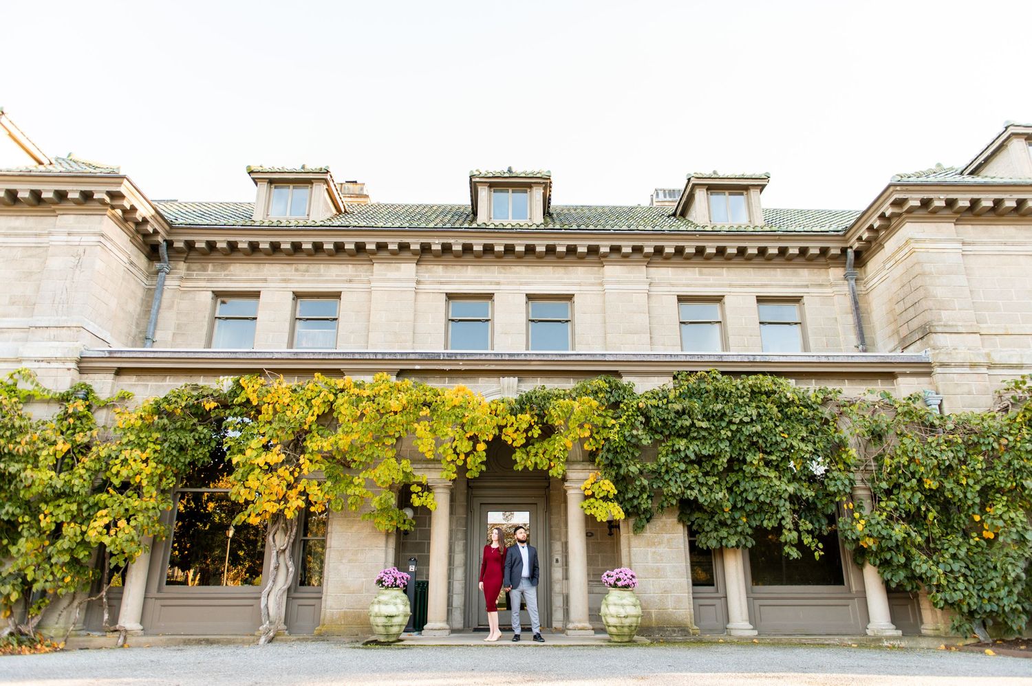 Stately stone mansion with yellow fall foliage and arched entrance.