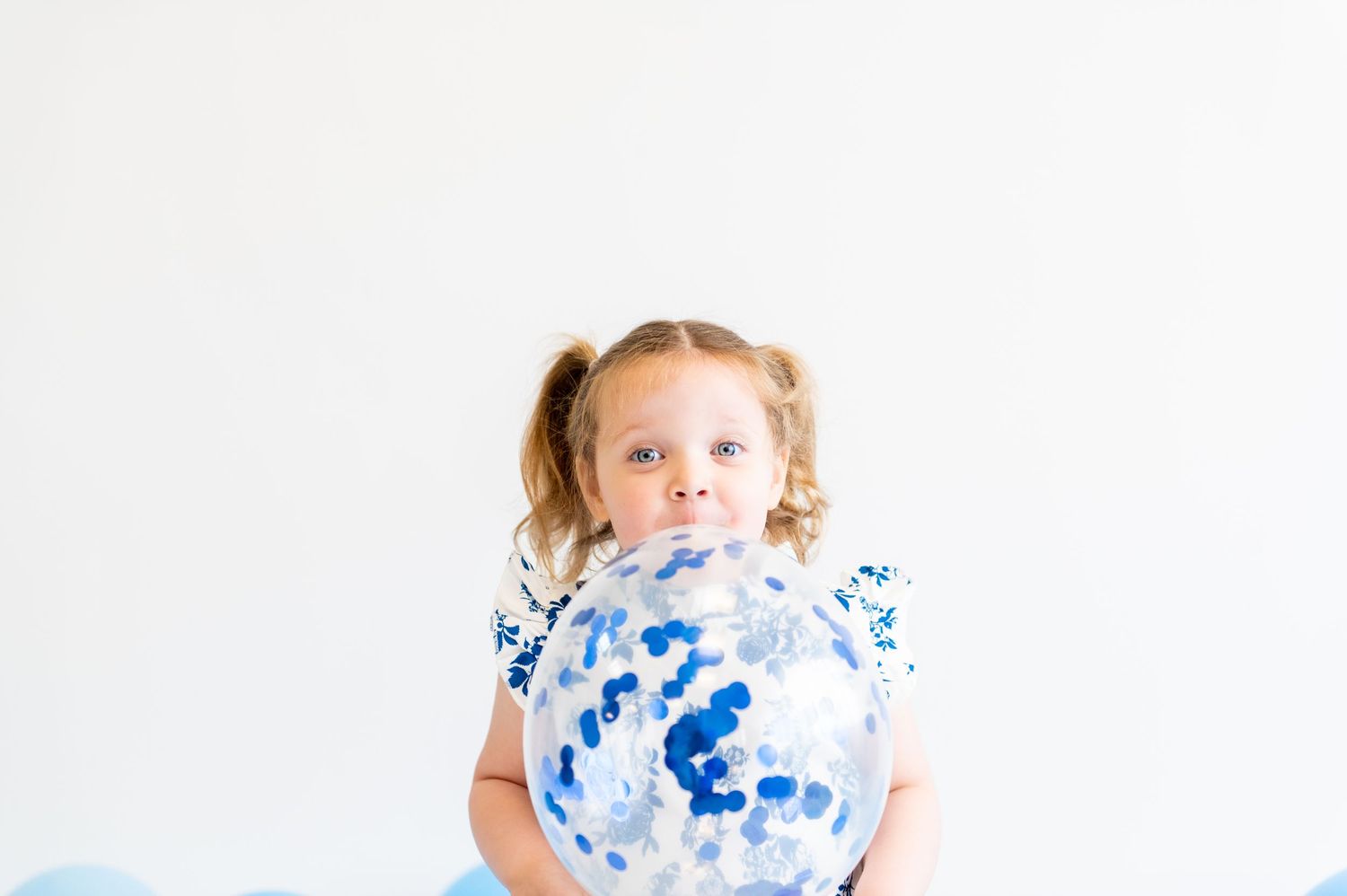 Child holding a large blue and white confetti balloon against white background.