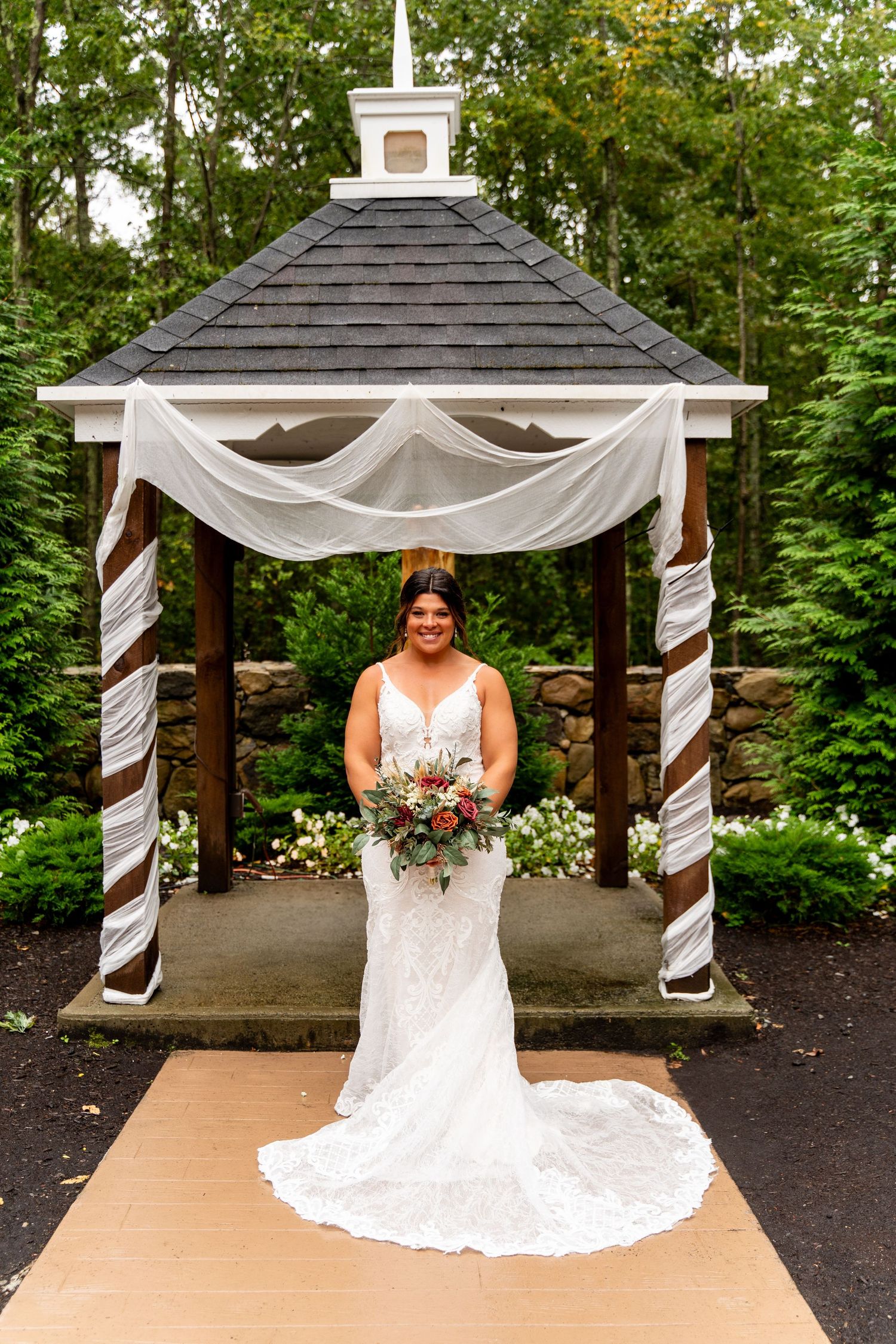 Elegant outdoor wedding gazebo decorated with white fabric and florals.