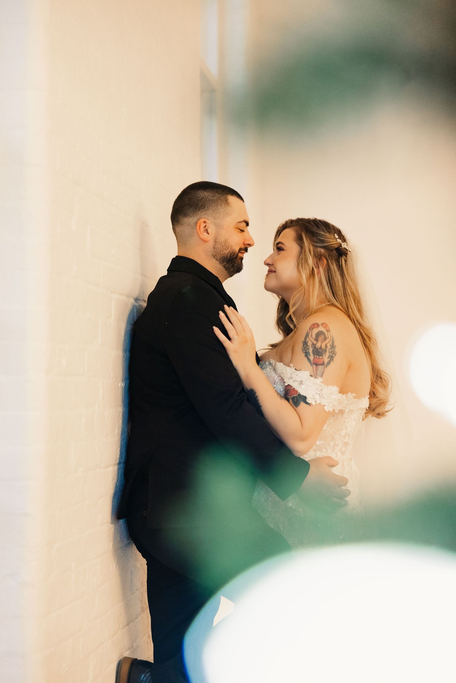 A romantic moment between newlyweds as they embrace against a white wall with Christmas decor.