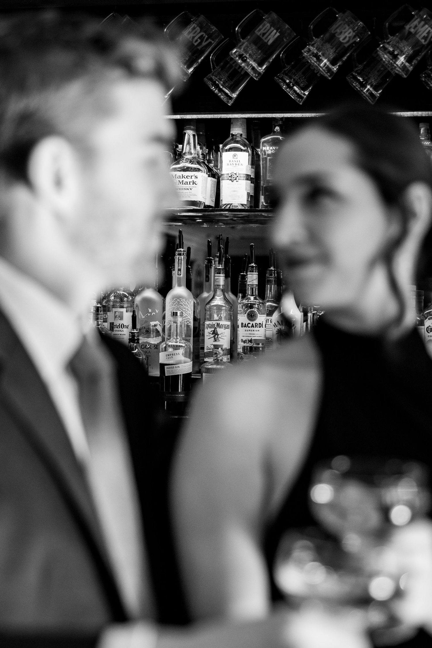 Black and white image of couple at bar with liquor bottles in background.