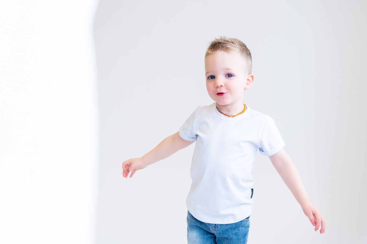 Child in white t-shirt and jeans stretching arms out against white background.