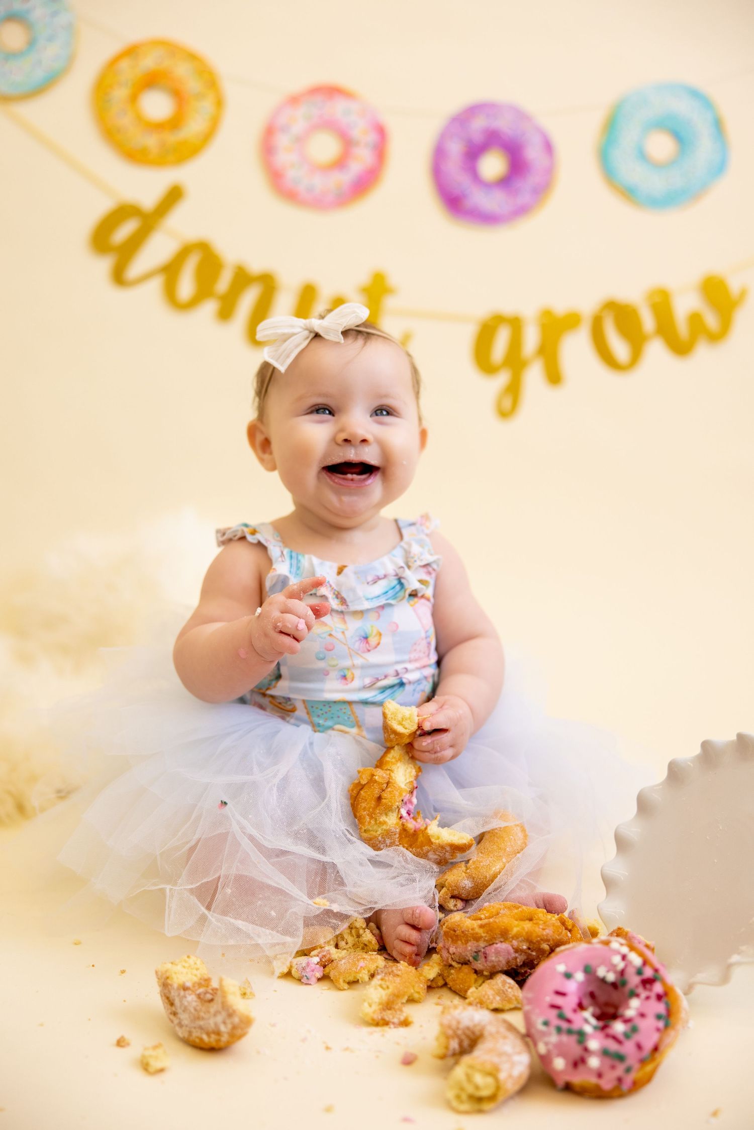 Baby in tulle outfit smiling with messy donuts during cake smash photo session.