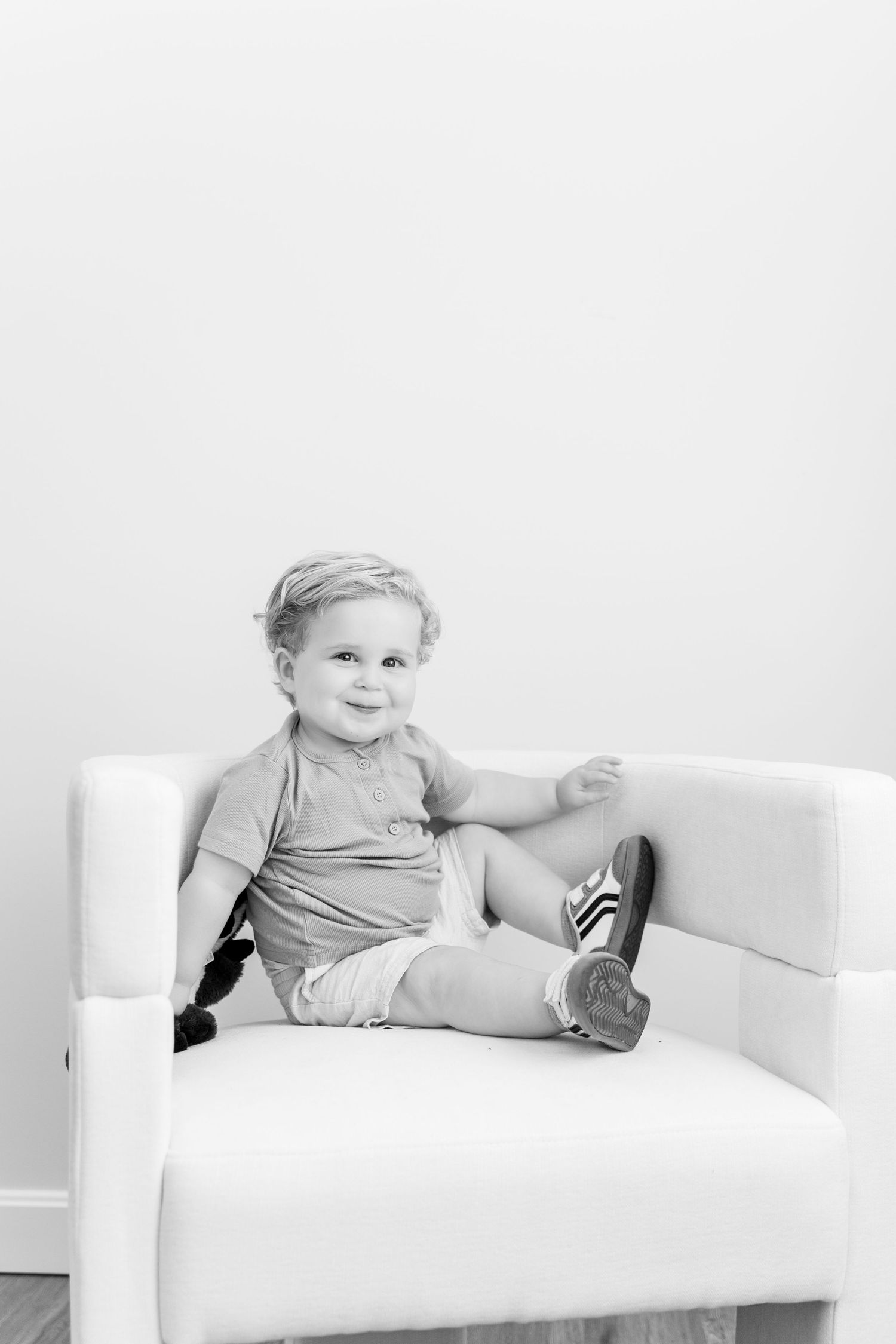 Child in gray outfit relaxing on white chair in black and white photo.