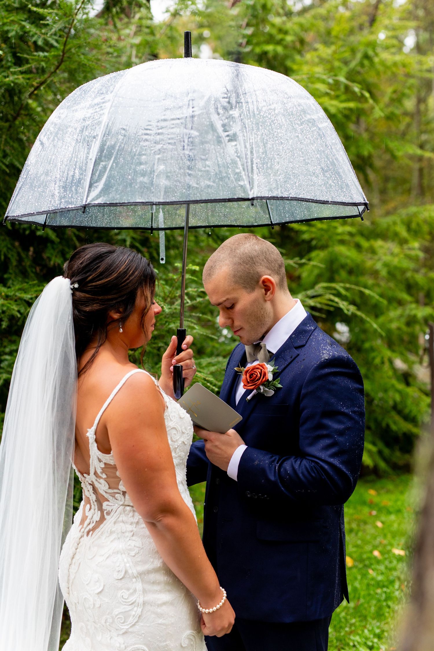 Couple exchanges vows under a clear umbrella during an outdoor ceremony.