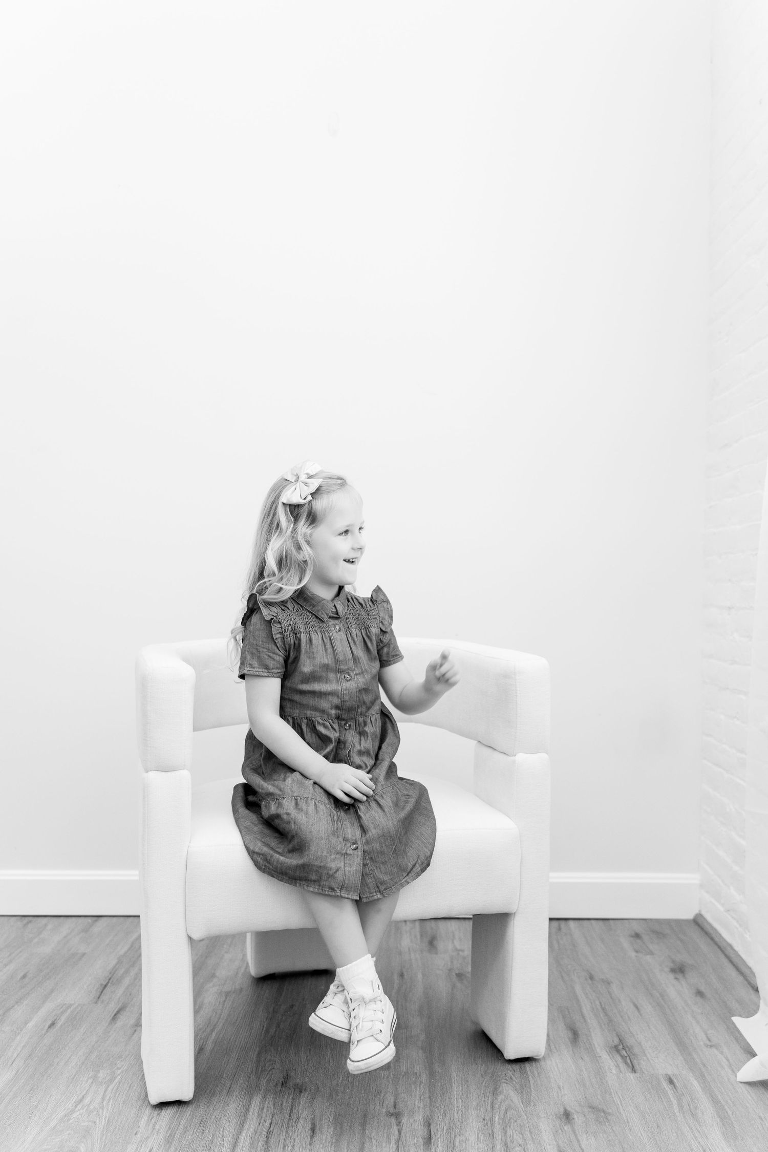 Child in gray dress sitting on white chair in minimalist setting.