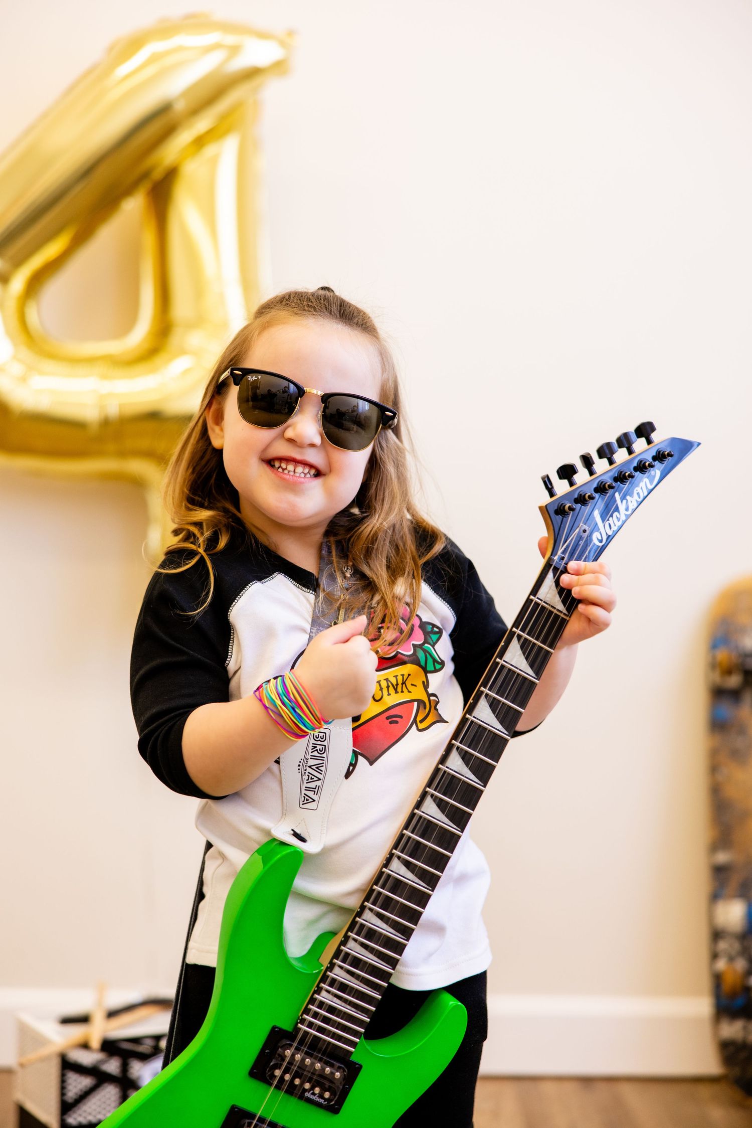 A young guitarist poses with a bright green electric guitar next to a gold number 4 balloon.