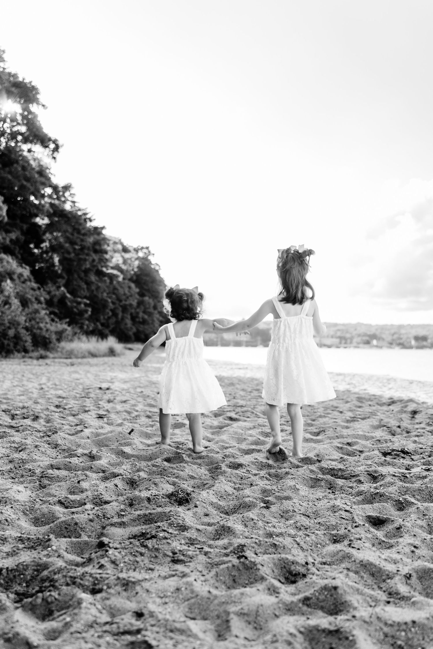 Black and white image of children holding hands while walking on beach.