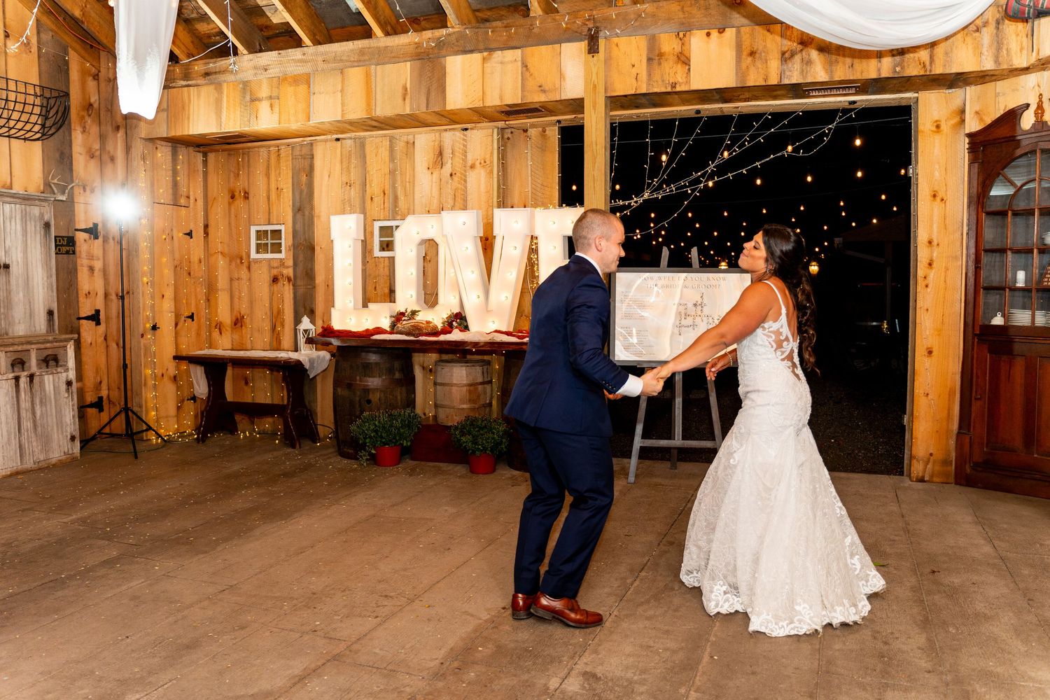 A couple dances in a rustic barn setting with white drapes and wooden walls.