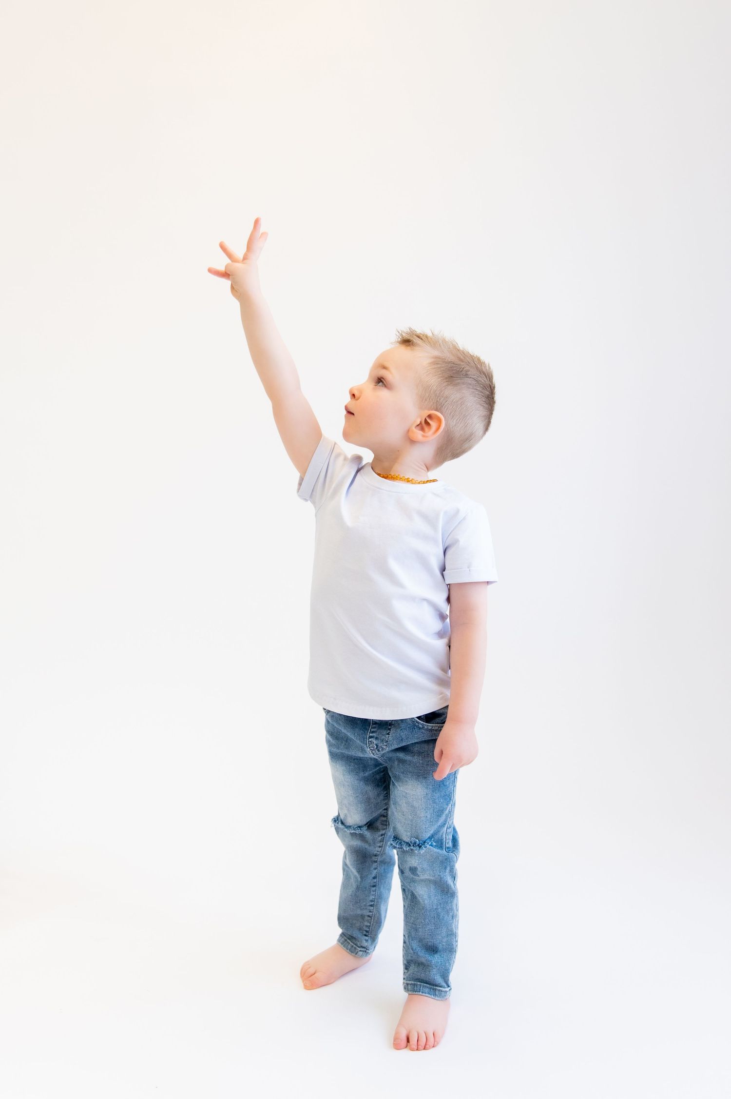 Child in white shirt and jeans reaching up with bare feet against white wall.