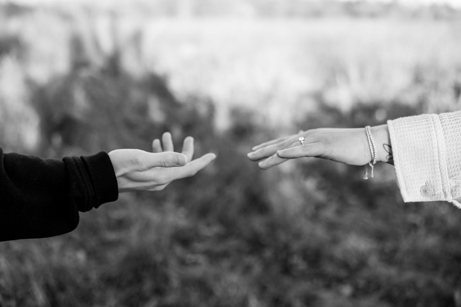 Black and white close-up of hands reaching toward each other with ring visible.