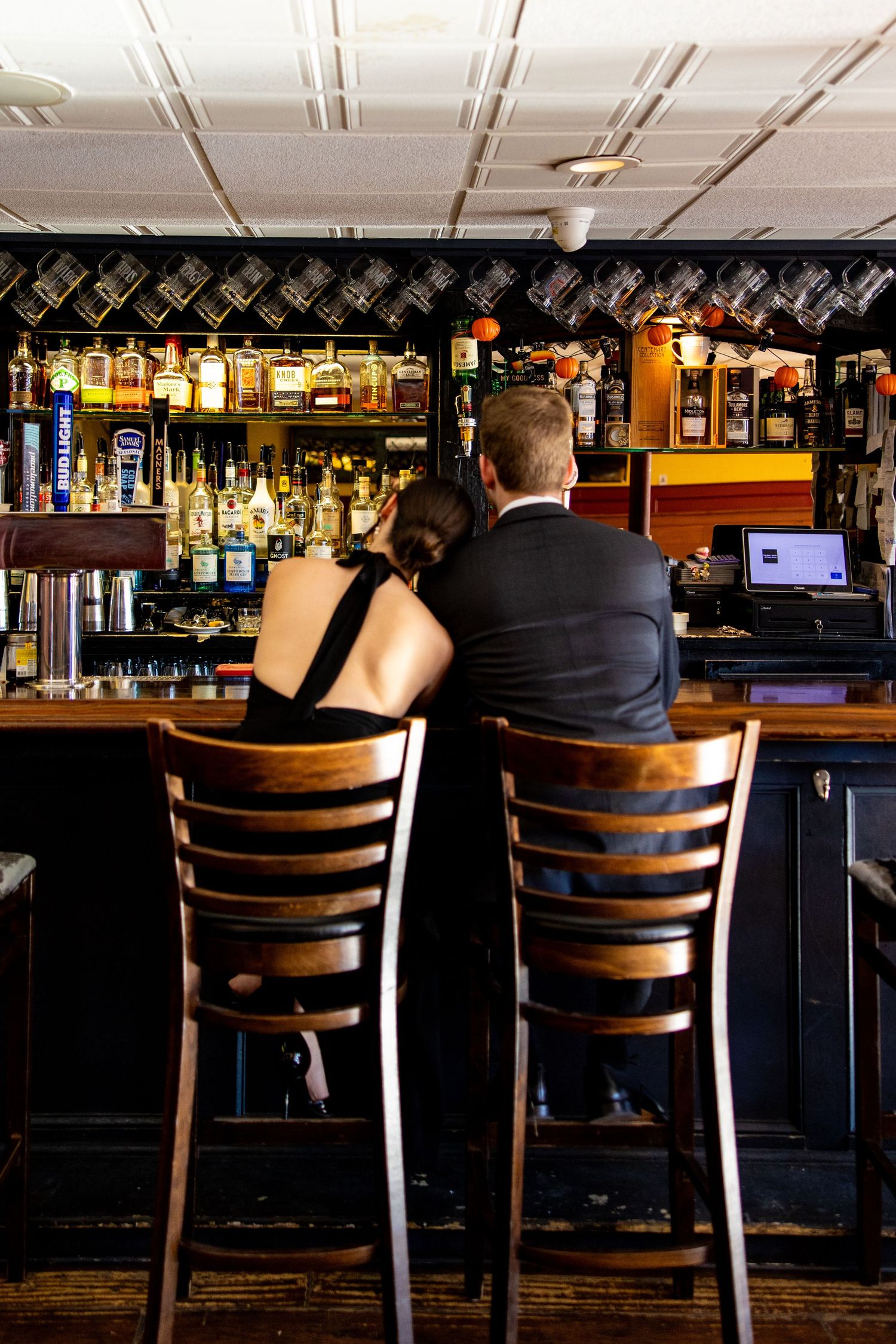 Couple sits at bar counter with extensive liquor bottle display behind them.