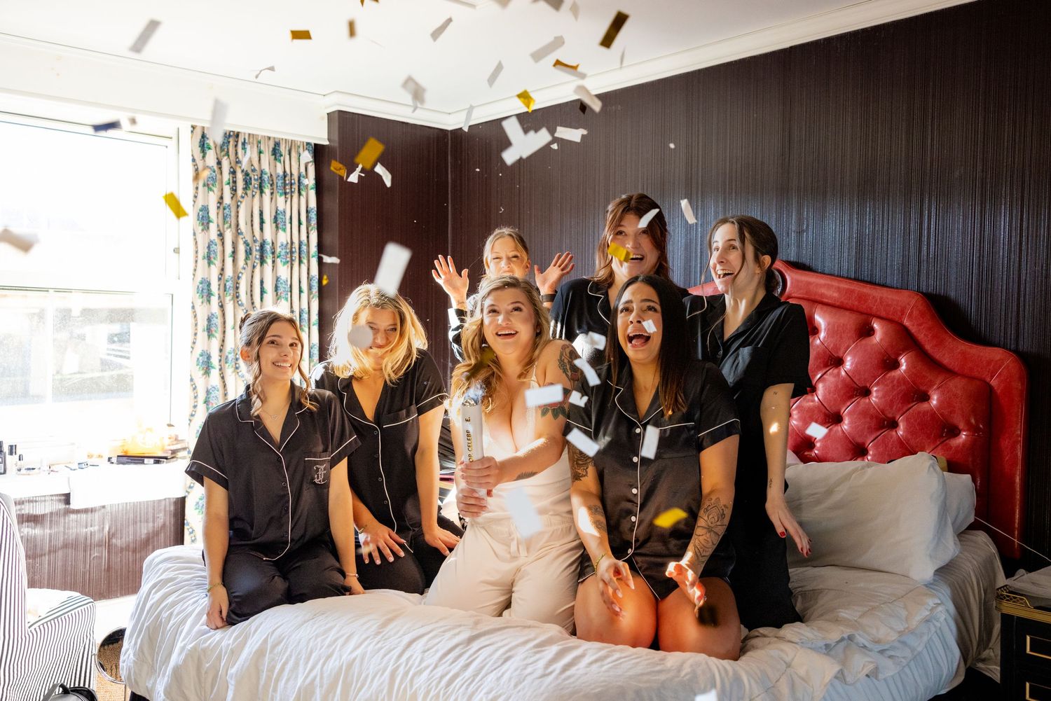 Wedding party celebrating on a bed with confetti flying through the air.