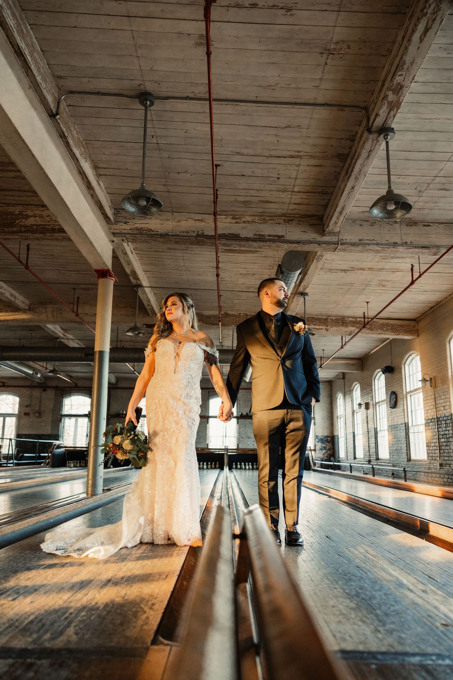 Wedding couple walks down vintage bowling alley in industrial chic venue with exposed ceiling.