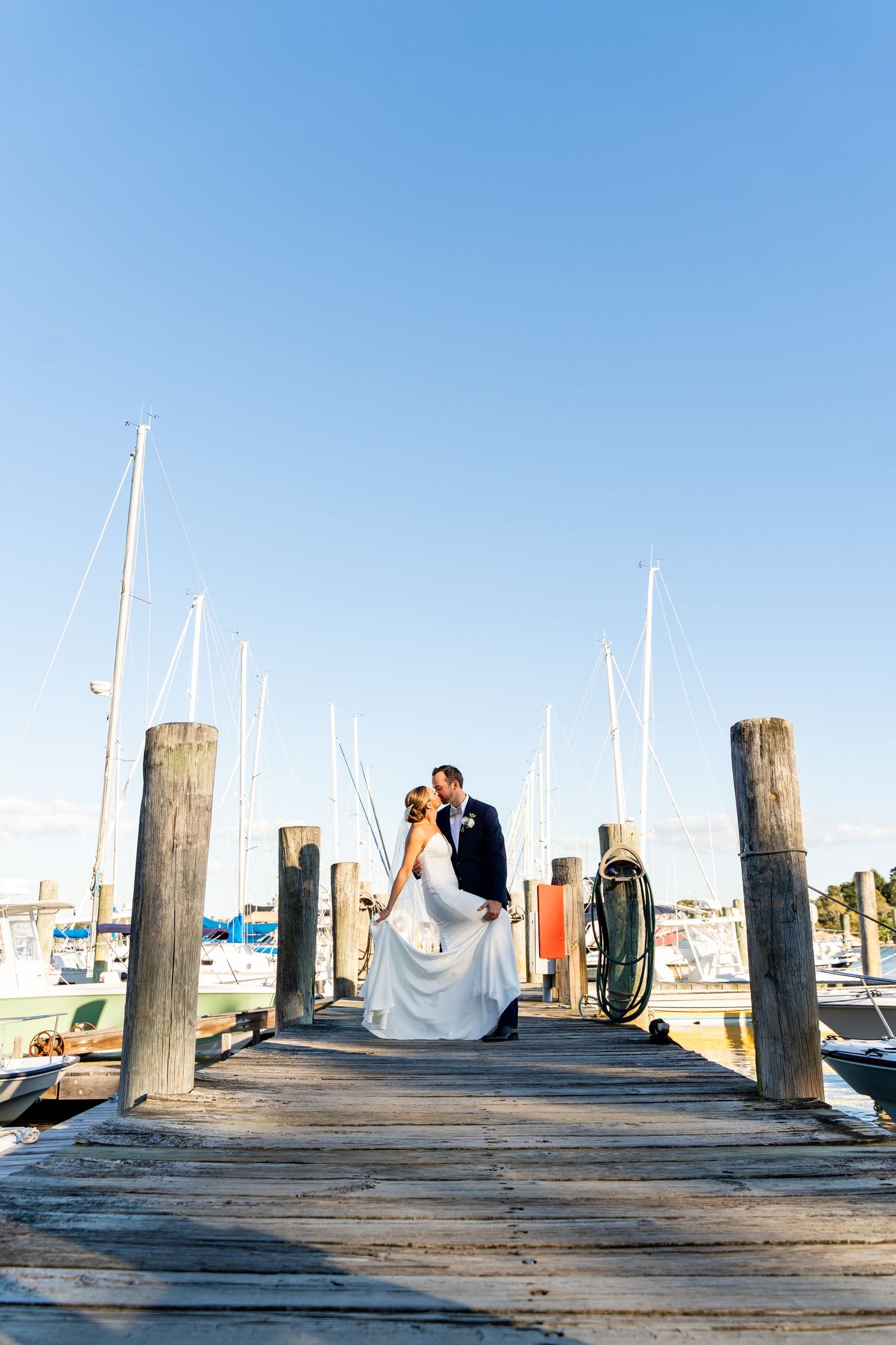 Newlyweds posing on wooden dock surrounded by boat masts.