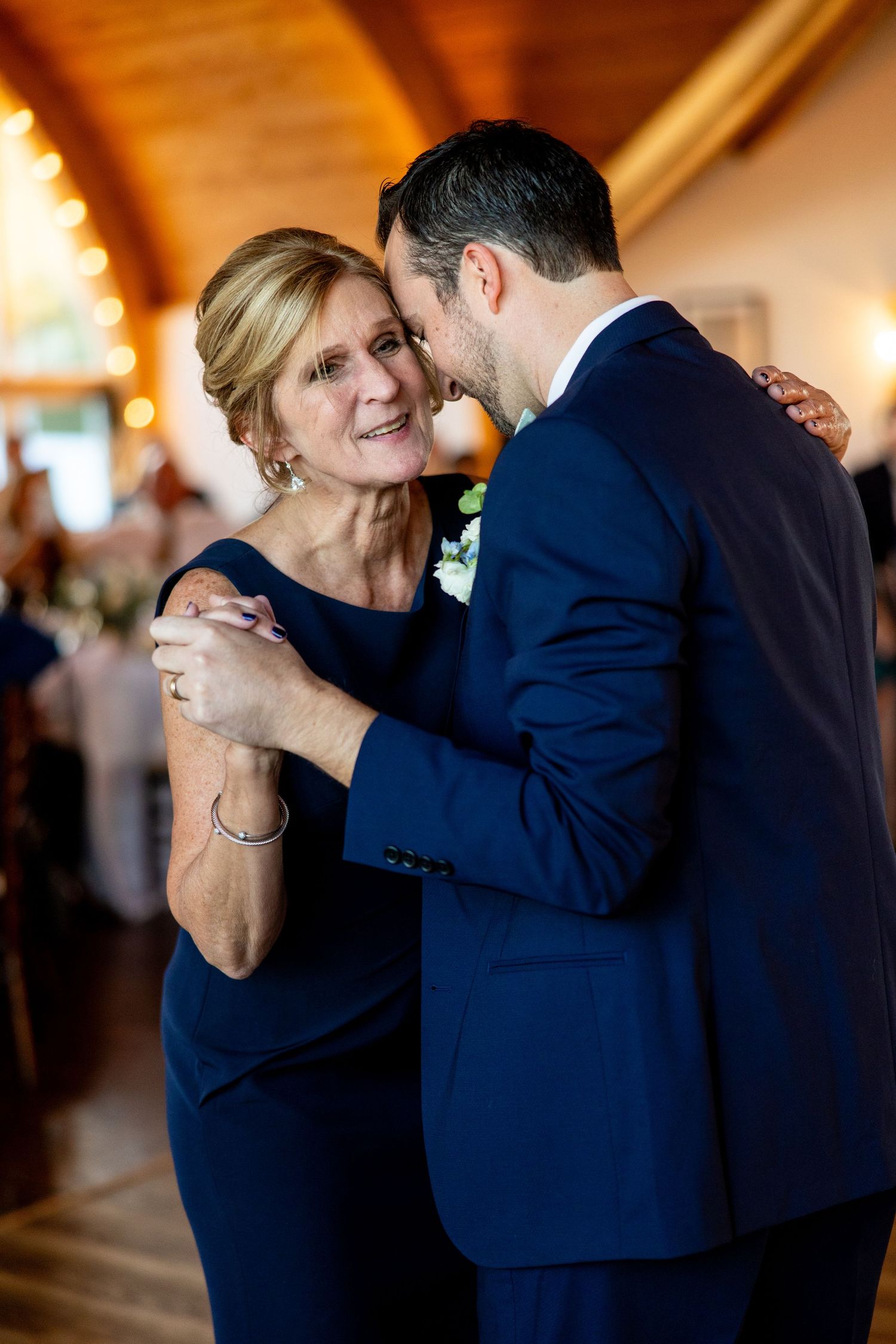 Intimate dance moment captured in warm-lit reception venue with wooden ceiling beams.