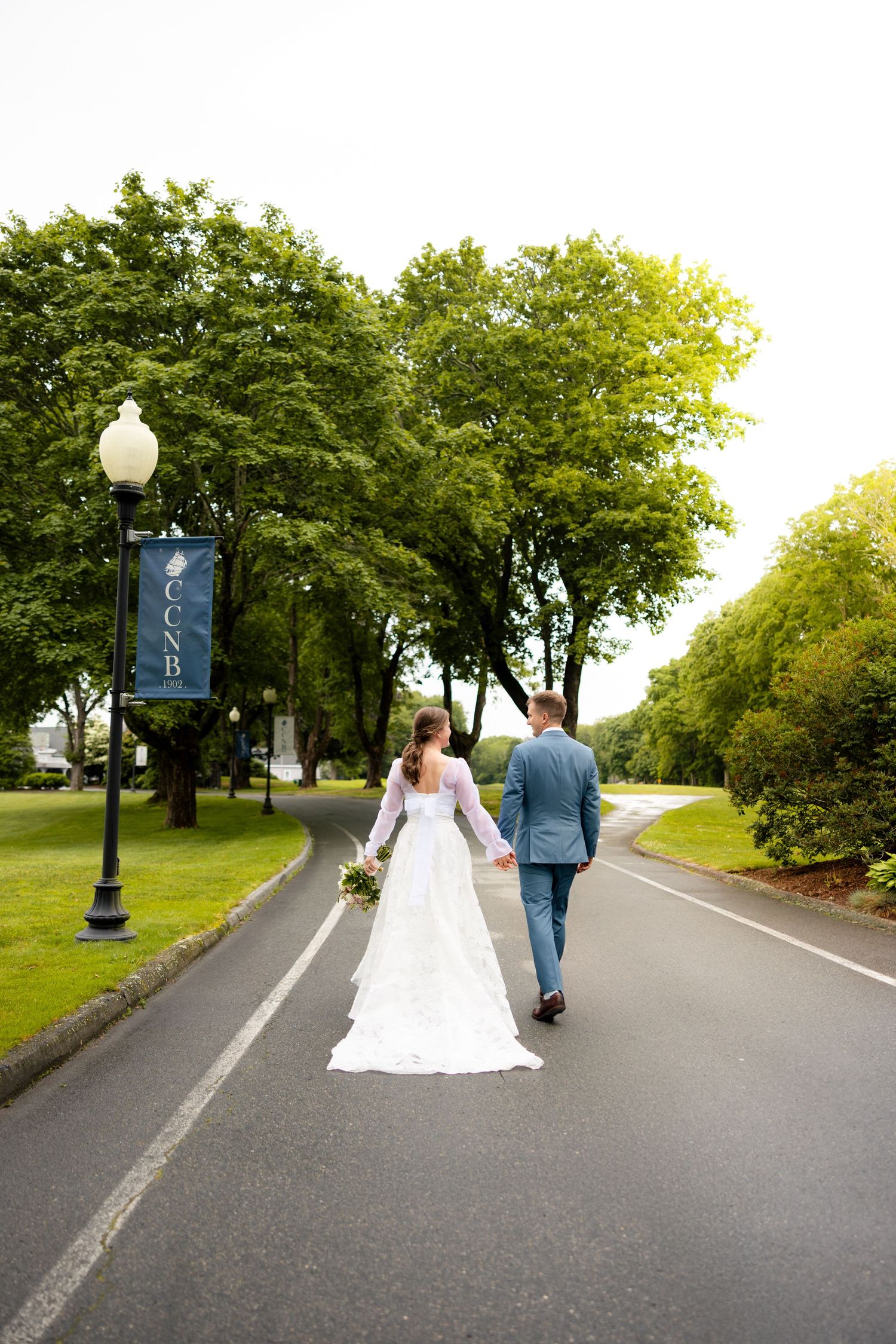 A couple in wedding attire walk together down a tree-lined path on their special day.