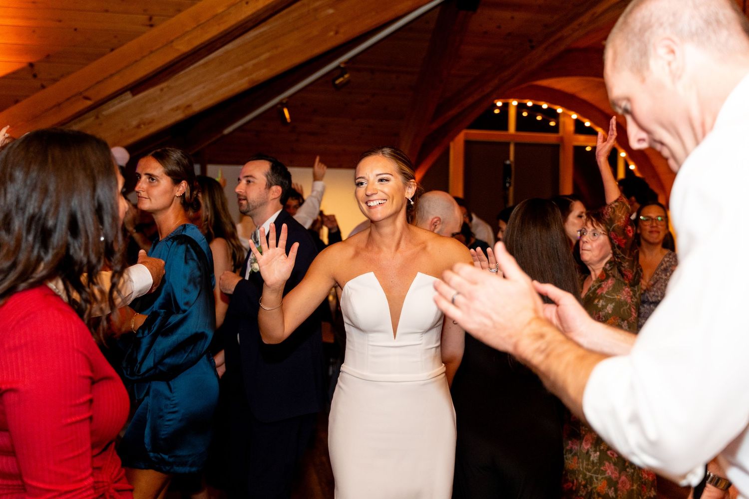 Wedding celebration with guests dancing in a rustic venue with wooden ceiling.