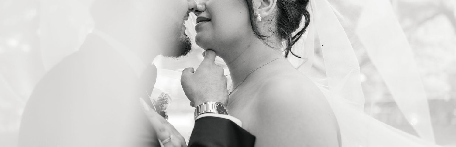Black and white photo of a bride and groom sharing an intimate moment, with the bride in a white gown and groom in a suit.
