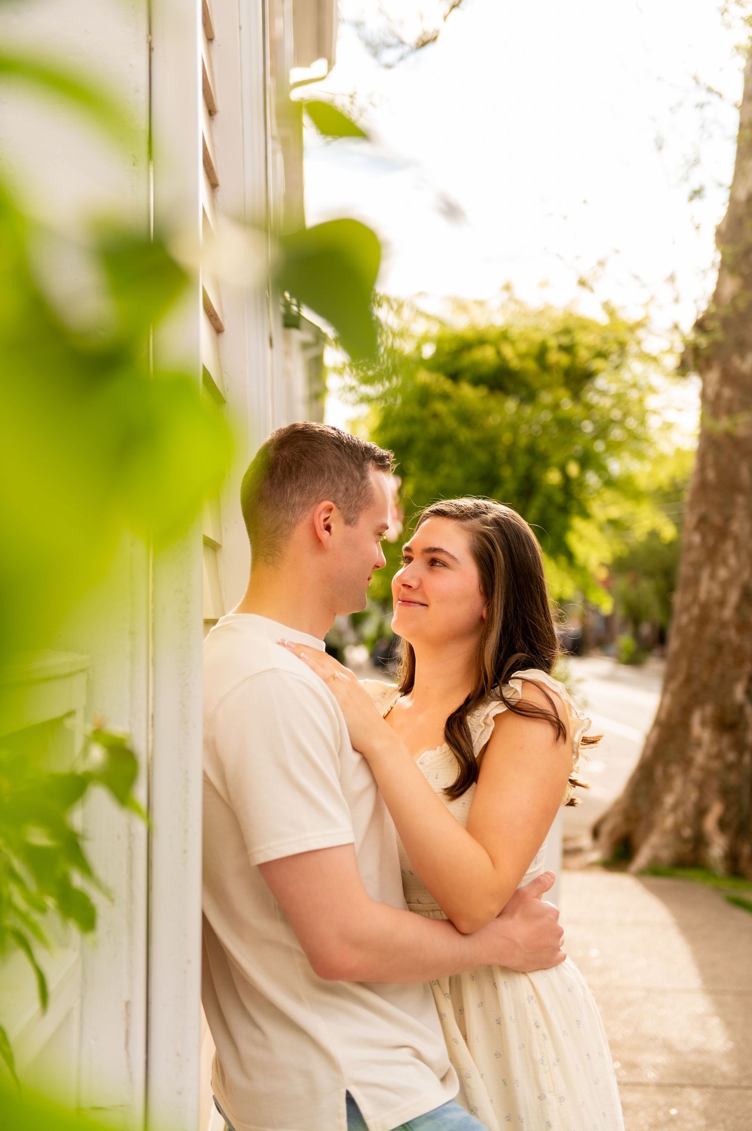 Romantic moment between couple against white wall with green foliage framing the scene.